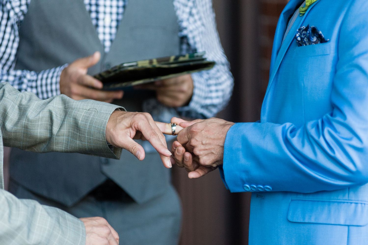 Groom in blue suit placing wedding ring on partners hand during ceremony.