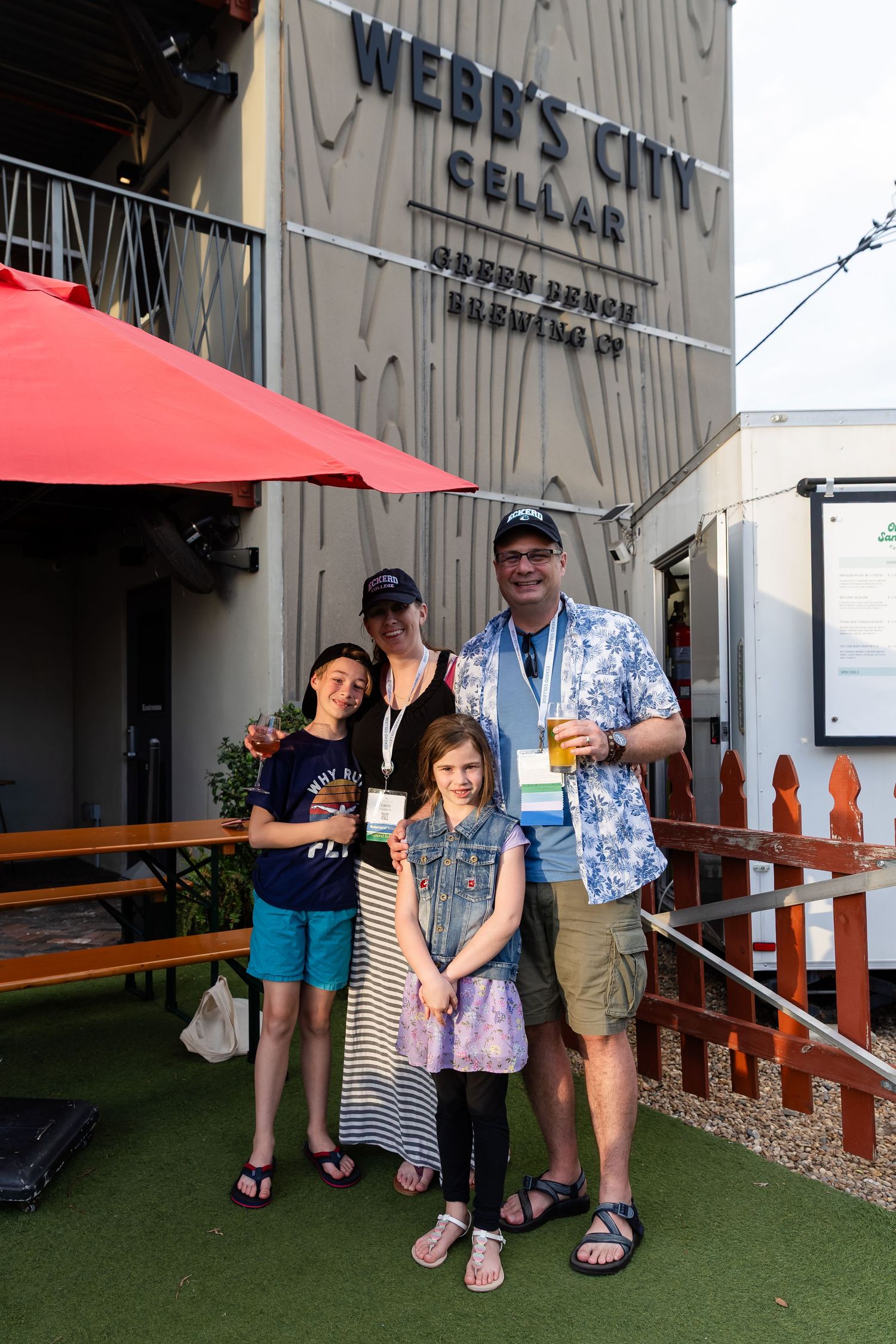 Family of four poses outside Webb's City Cellar Green Bench Brewing Co on a sunny day.