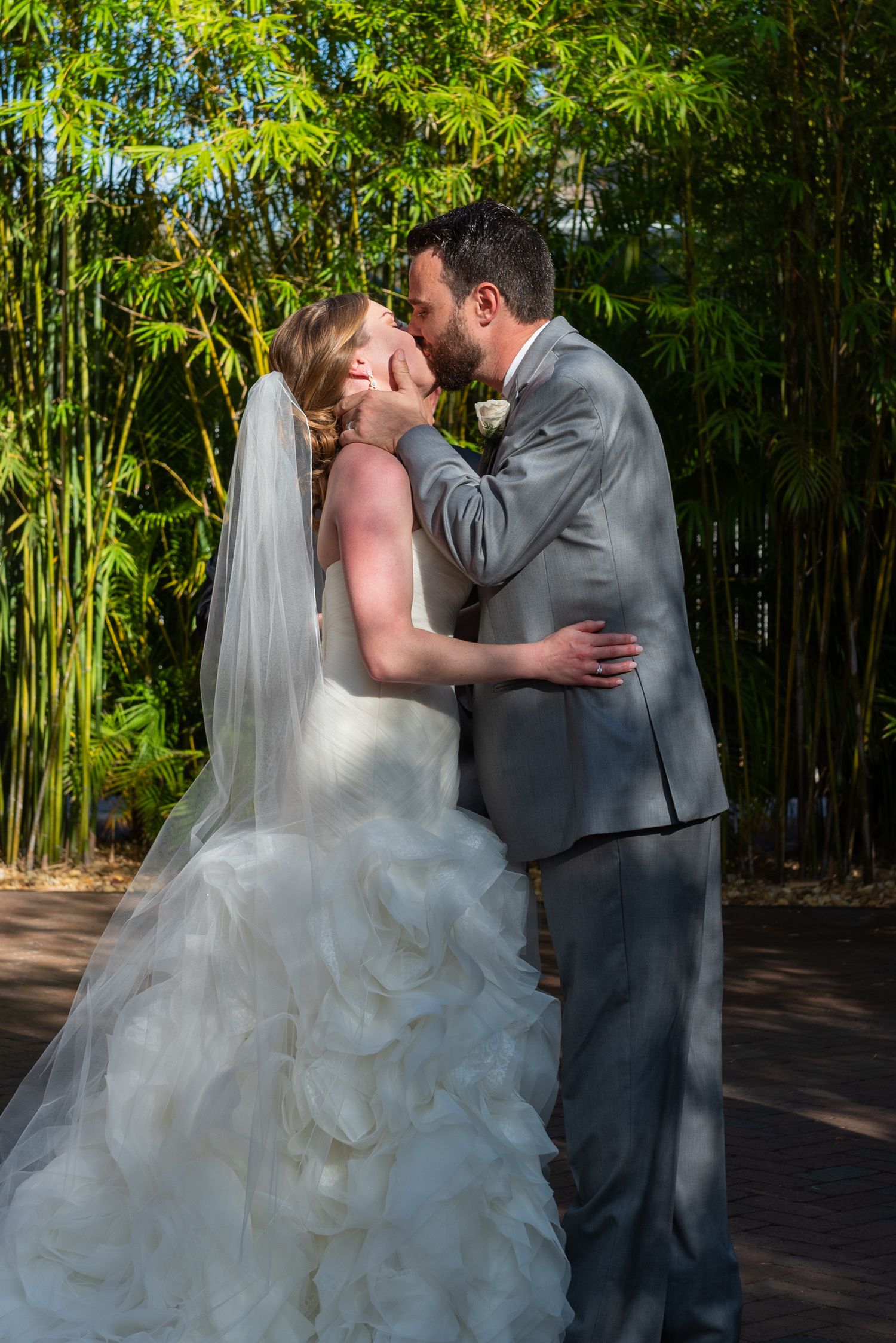 Bride and groom share a romantic kiss outdoors surrounded by lush bamboo trees during their wedding ceremony.