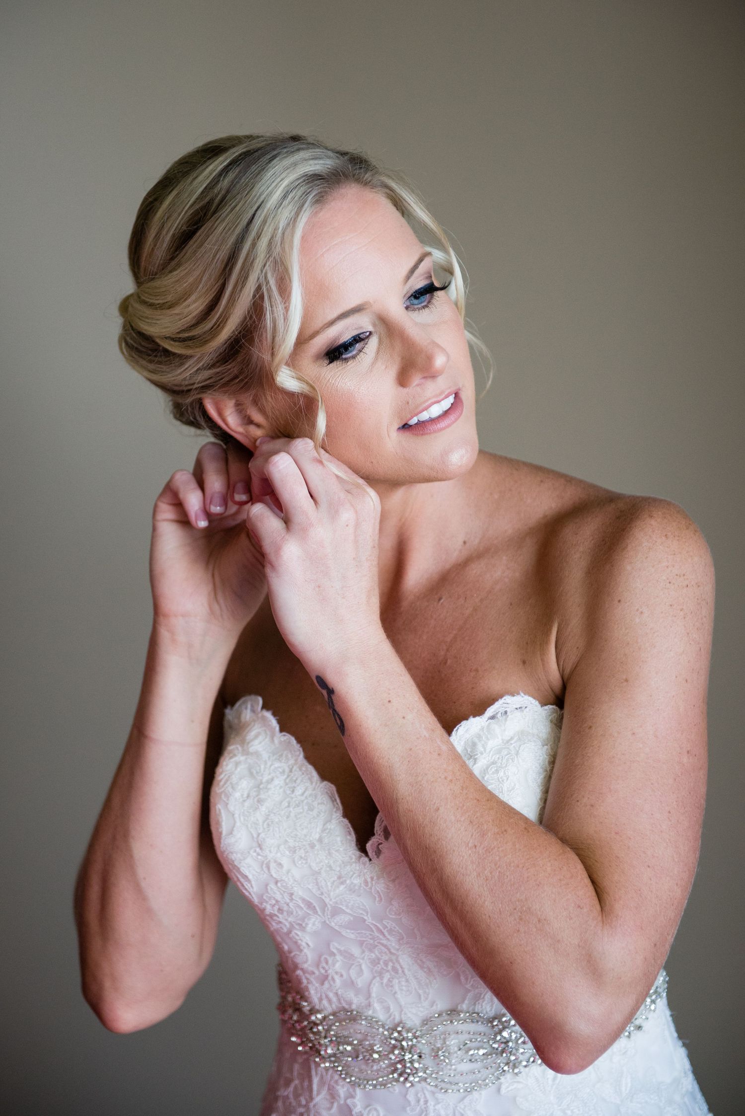 Bride in strapless lace wedding gown putting on earrings while getting ready for her wedding day.