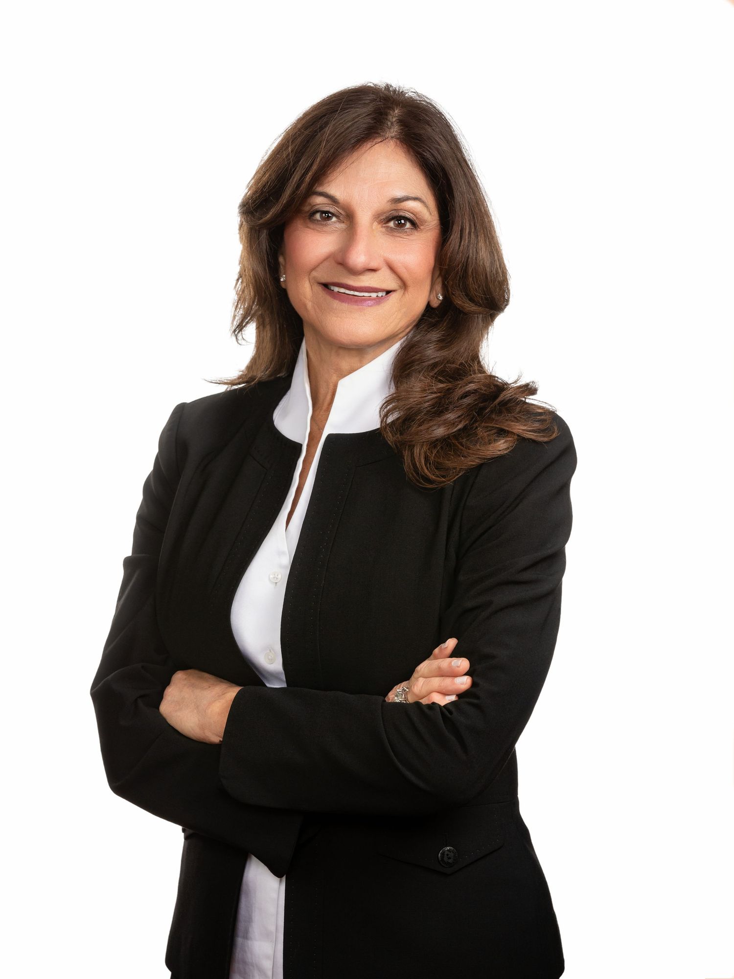Professional woman in black blazer and white shirt, arms crossed, smiling confidently against white background.