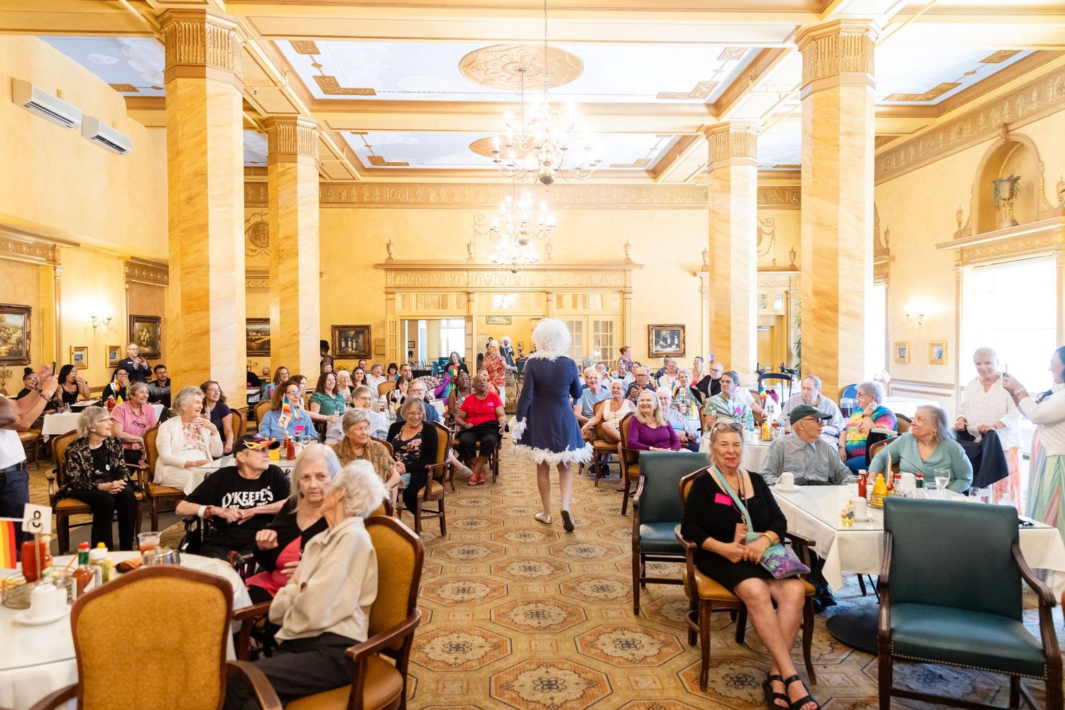 Elegant ballroom event with guests seated at tables during a fashion show in a grand ornate venue.