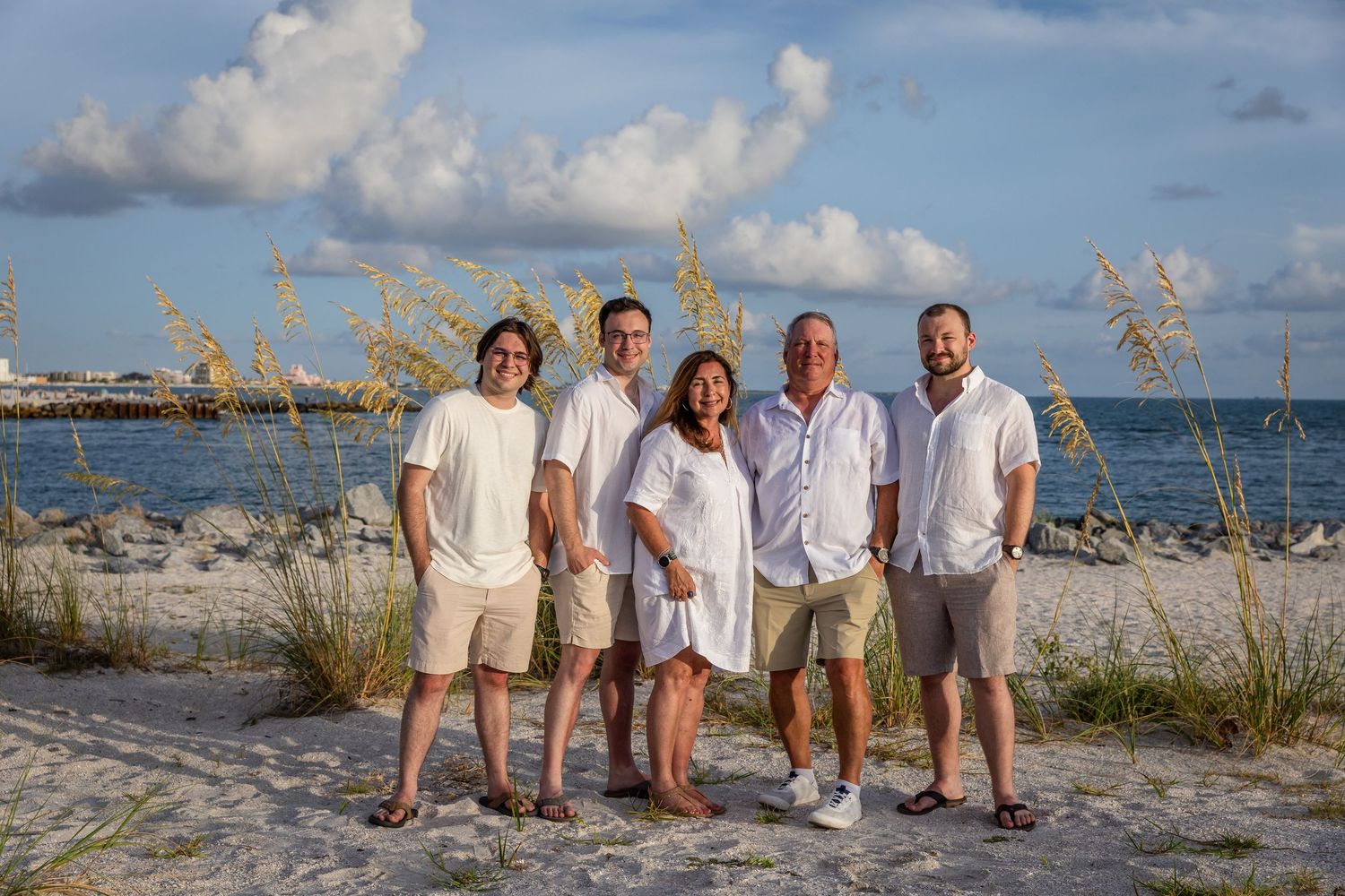 Family of five posing together on a sandy beach with sea oats and blue skies in the background.