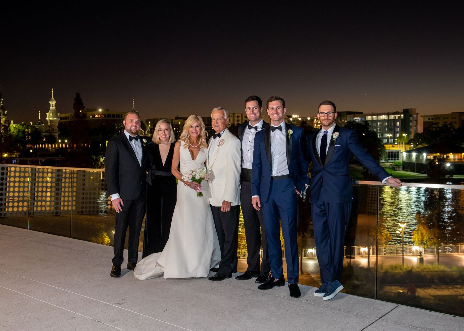 Wedding party poses on rooftop terrace at night with illuminated cityscape and waterfront in background at Tampa museum of fine art.