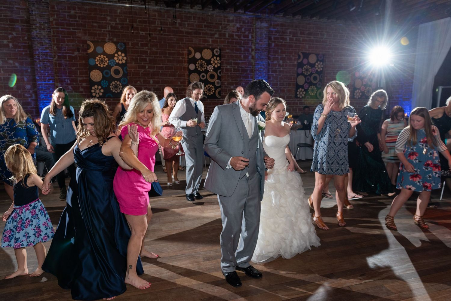 Bride and groom dancing with wedding guests on a decorated reception dance floor during a lively celebration.