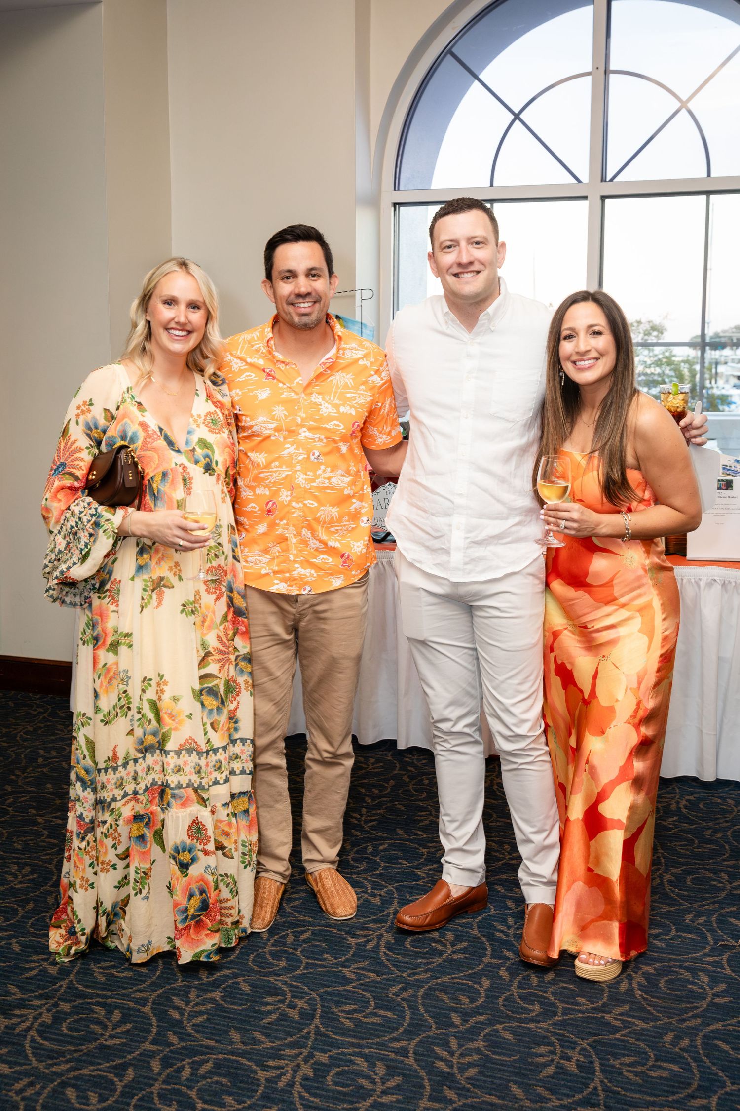 Four guests in tropical attire smile together at an elegant waterfront event venue.