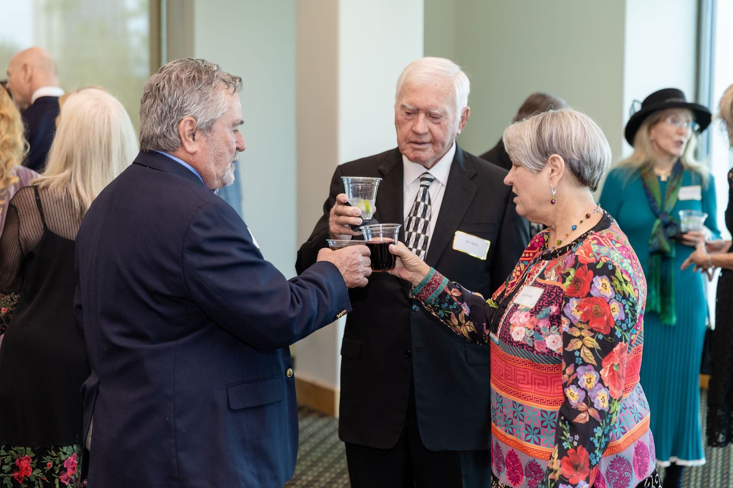 Three elegantly dressed seniors toasting drinks at a formal networking event or gala reception.