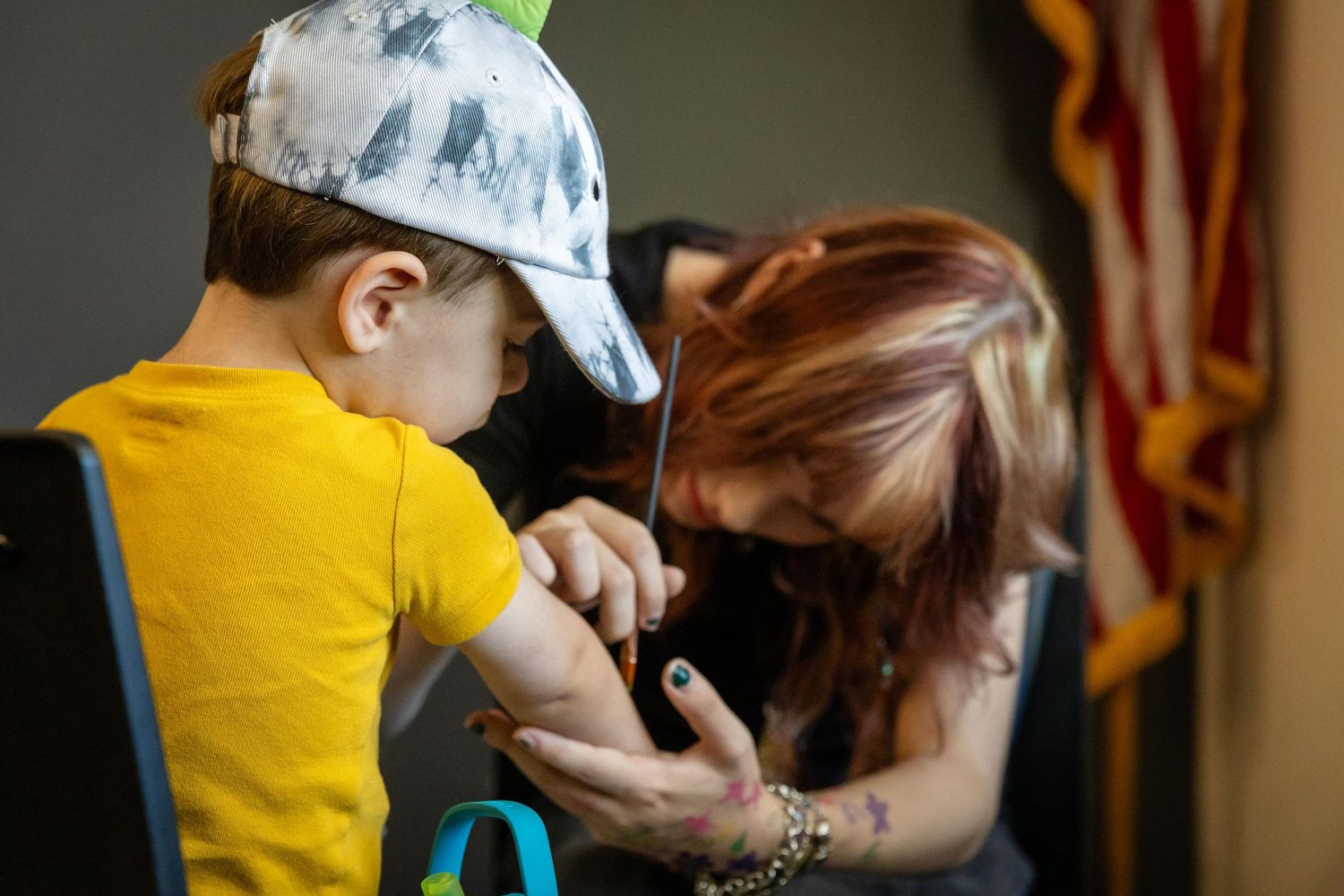 A healthcare worker administers a vaccine to a young boy wearing a yellow shirt and cap.
