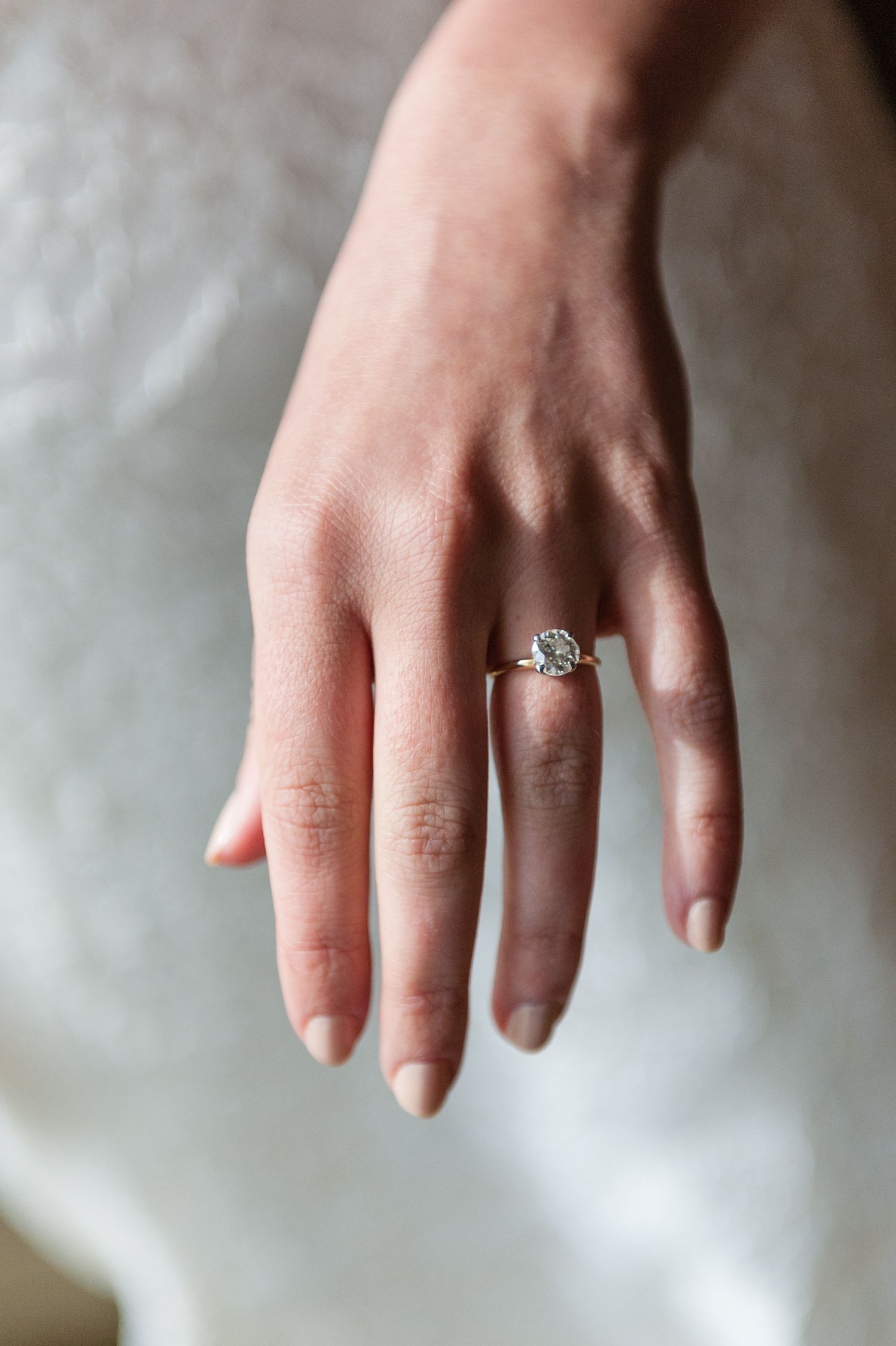 Close-up of a bride's hand displaying a stunning solitaire diamond engagement ring on her wedding day.