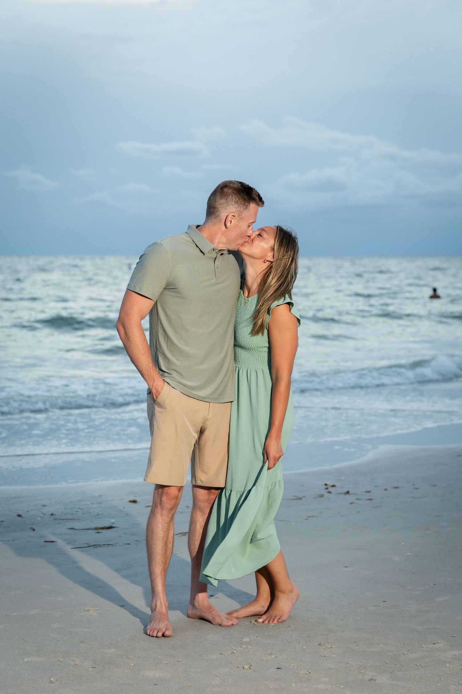 Romantic couple sharing a kiss on sandy beach at dusk, waves in background.