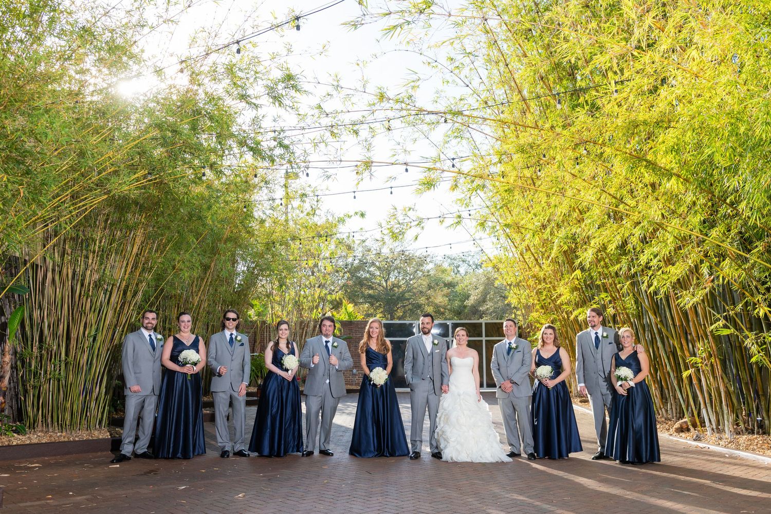 Wedding party poses together in bamboo garden with string lights overhead.