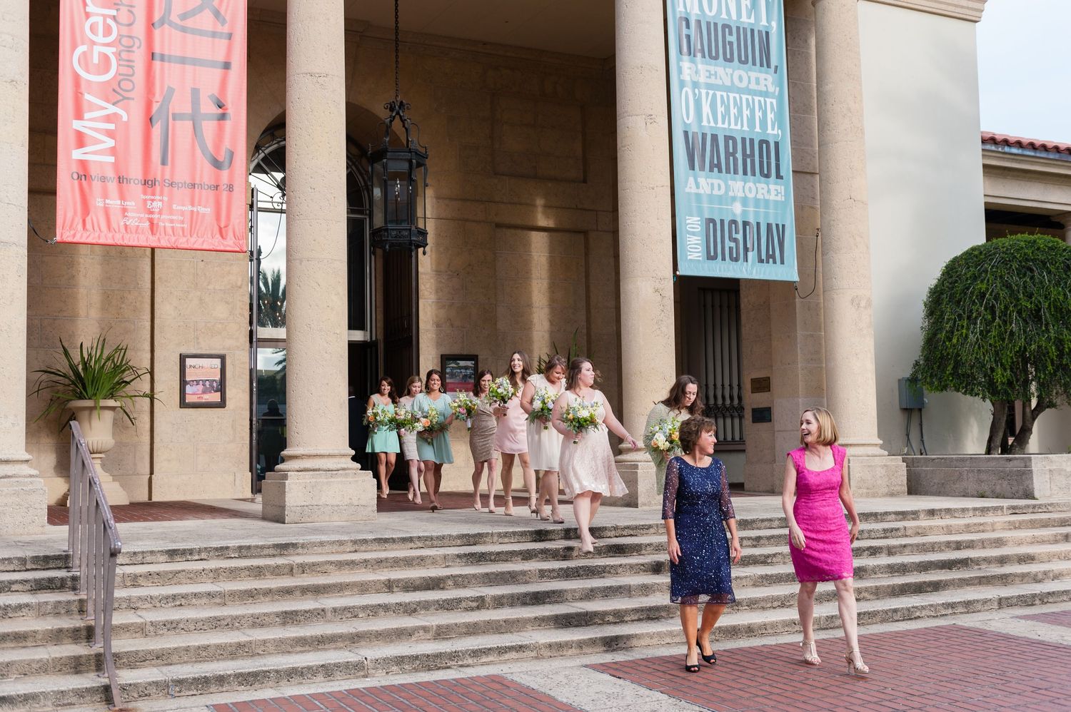 Wedding party descending steps of art museum entrance with bridesmaids holding bouquets outdoors Museum of Fine Arts, St. Petersburg.