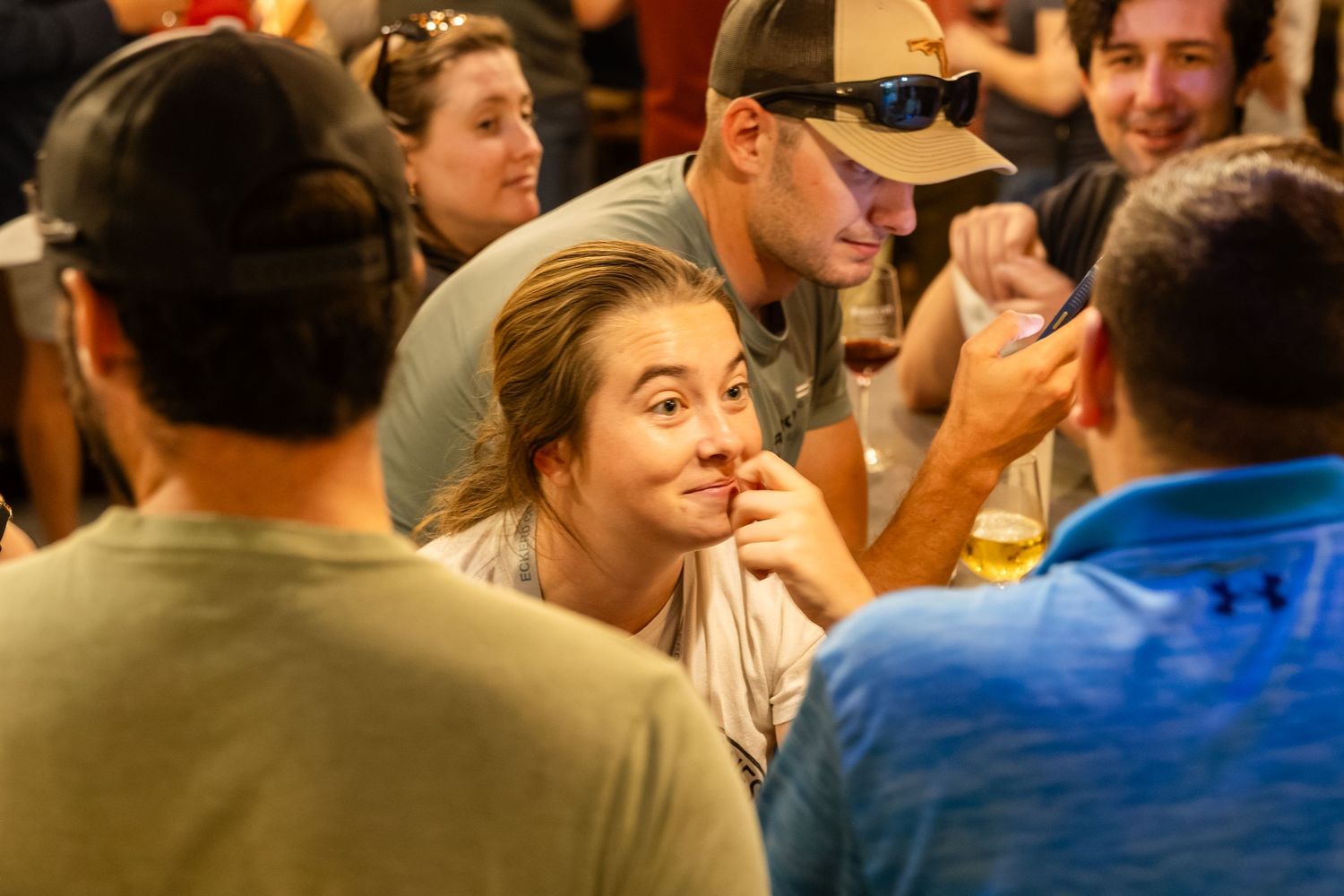 Young woman smiling and chatting with friends at a lively indoor social gathering, holding a drink.