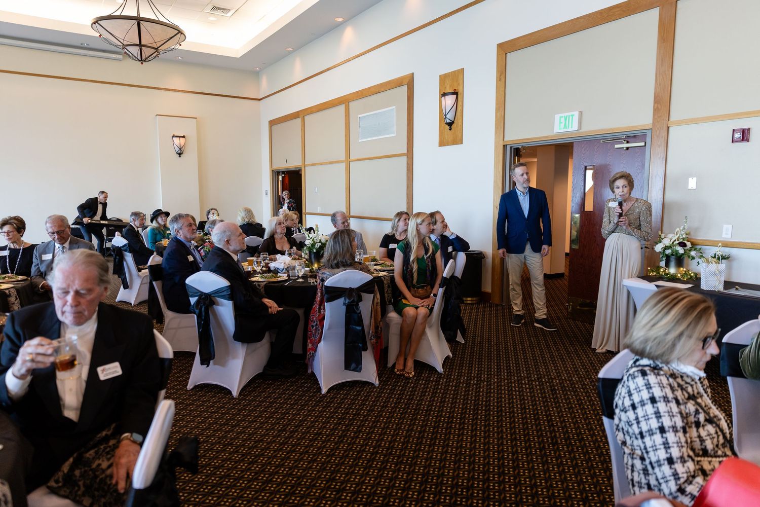 Guests seated at elegantly decorated tables during a formal banquet event in a carpeted ballroom.