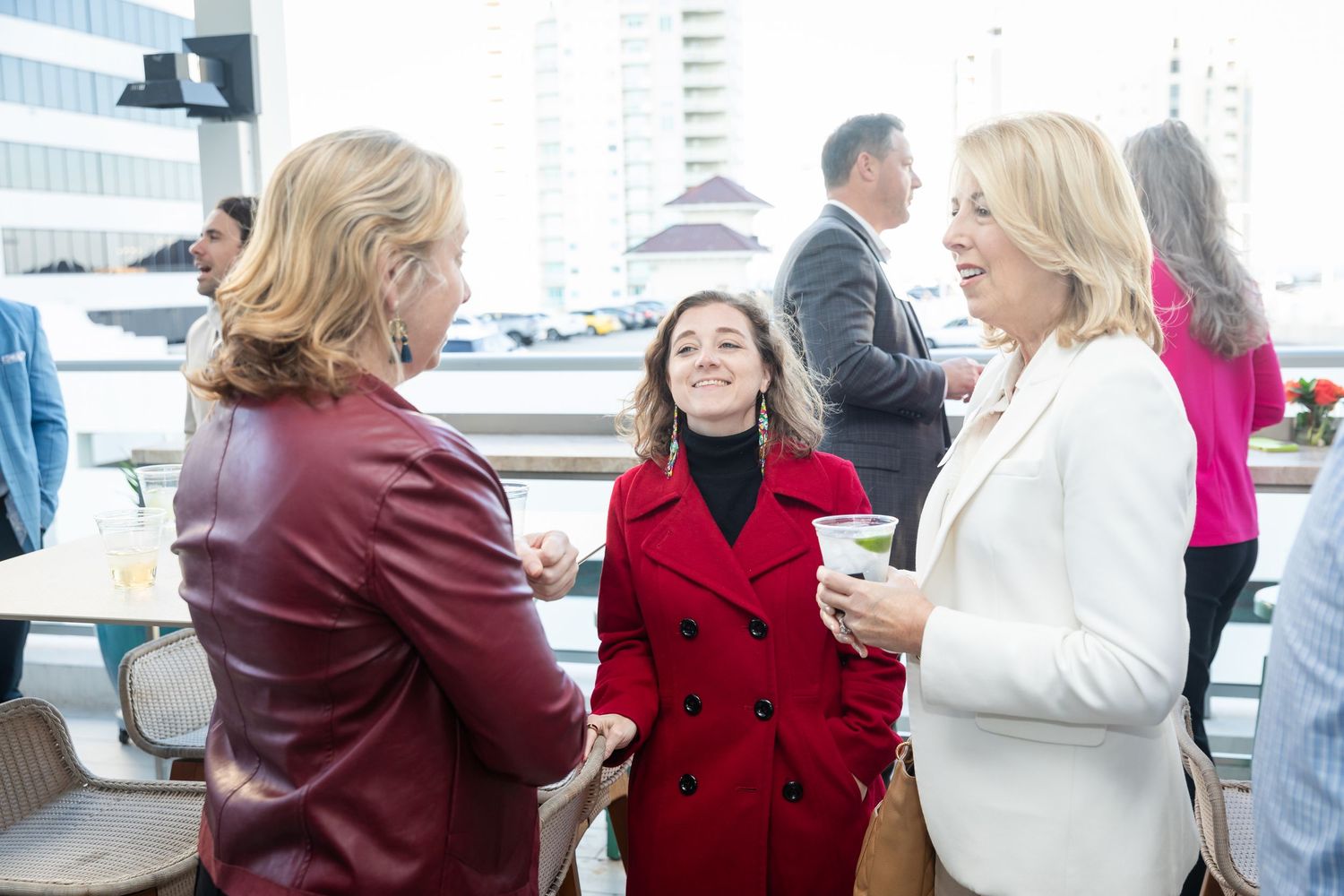 Three women in colorful coats socializing at an outdoor rooftop corporate networking event.