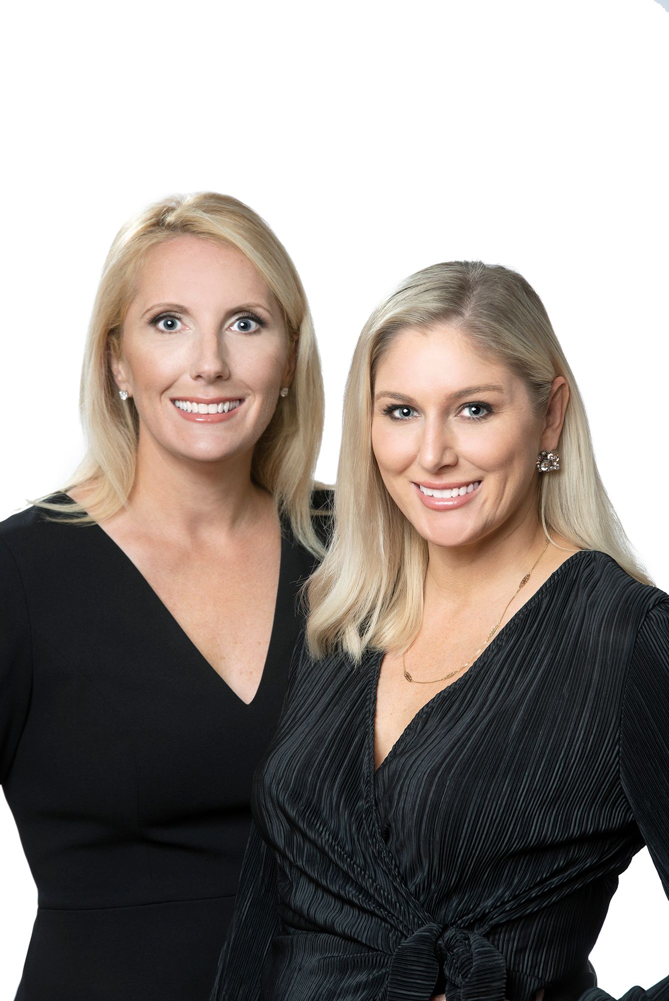 Two smiling blonde women in black outfits pose together against a white background for a professional portrait.