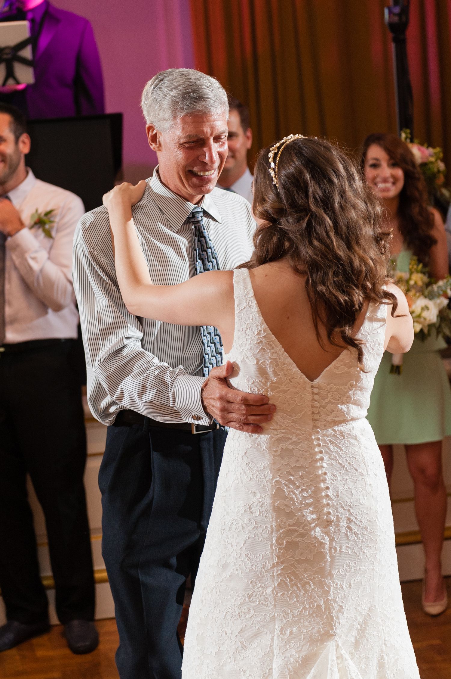 Bride shares emotional father-daughter dance at wedding reception with guests watching.