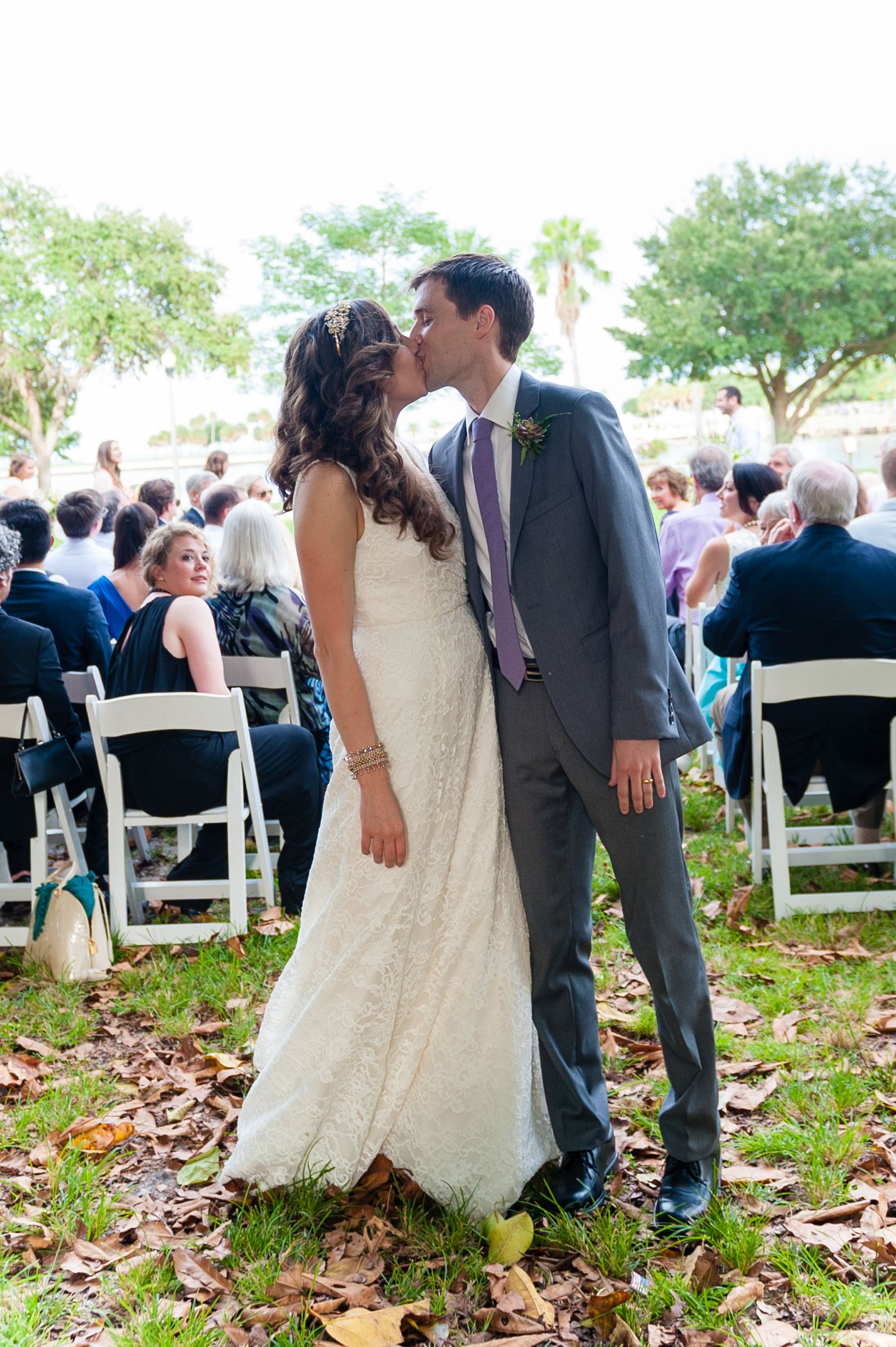 Bride and groom share a kiss at outdoor wedding ceremony with guests seated on white chairs.