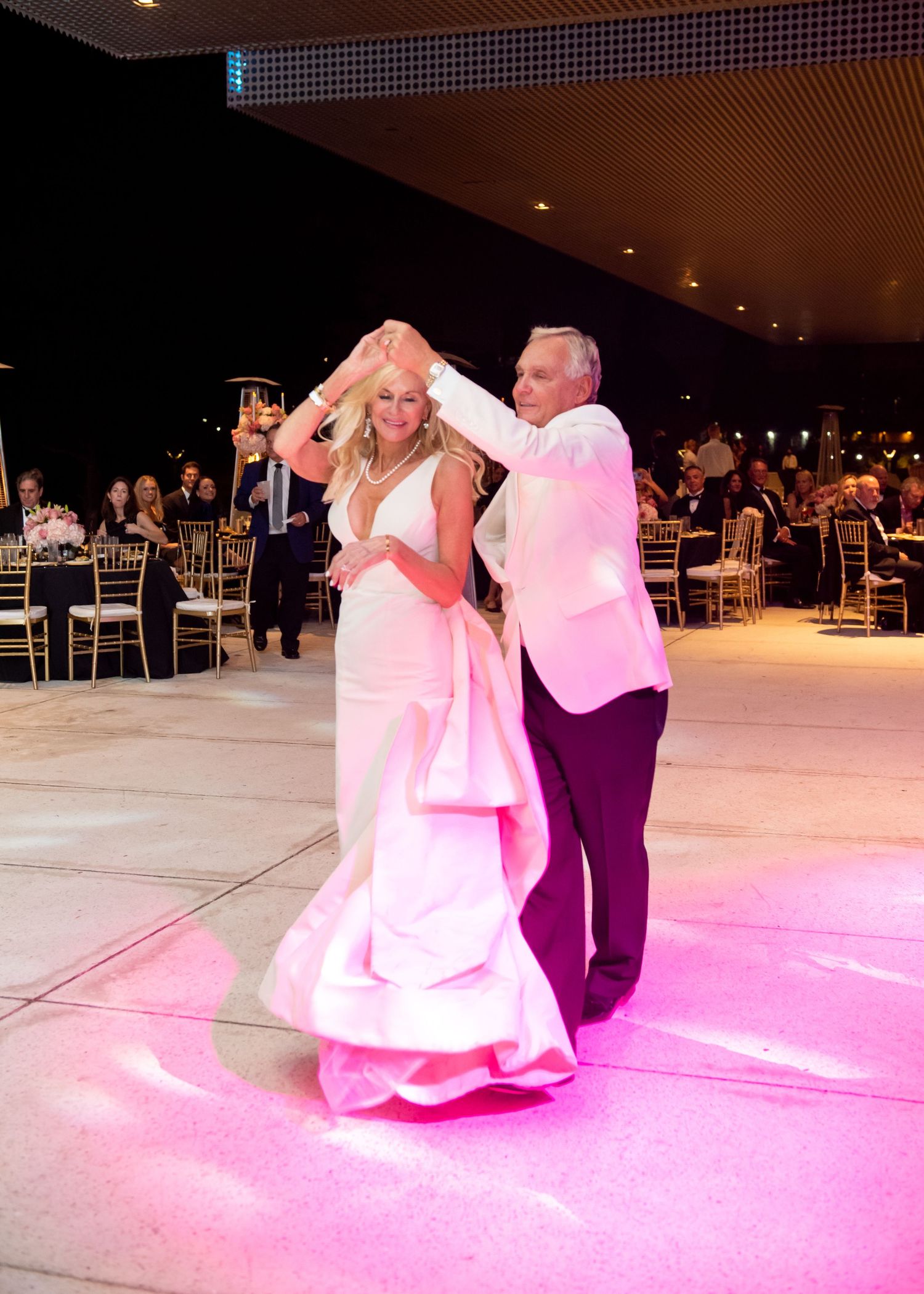 Bride and father share elegant first dance on pink-lit floor at upscale wedding reception.