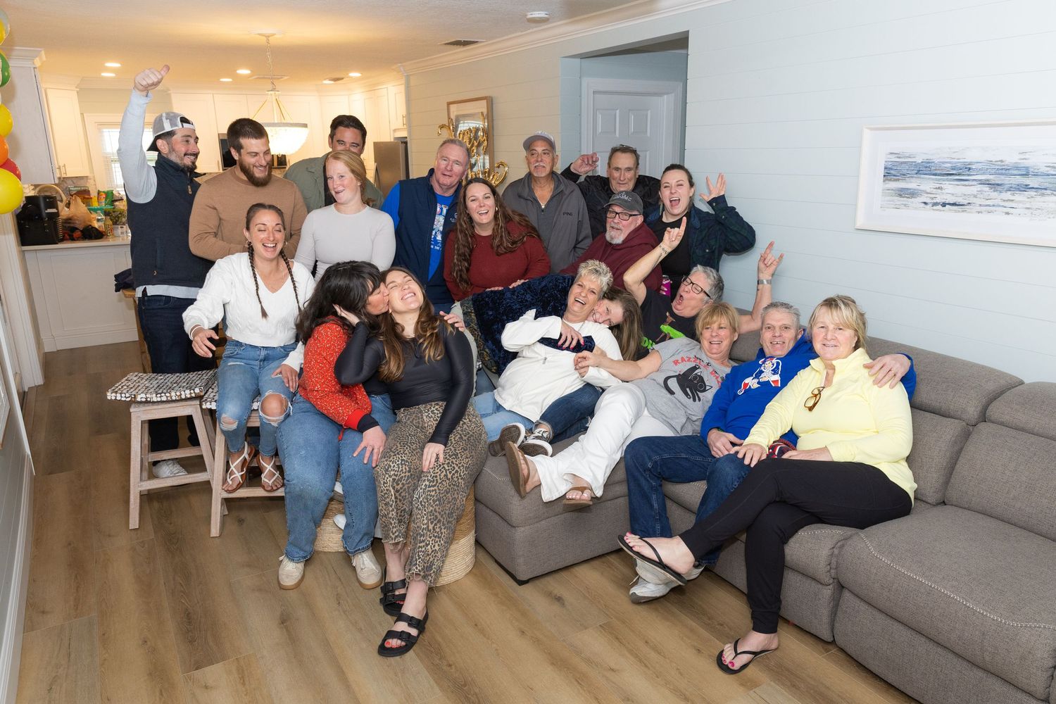 Large group of smiling friends and family posing together in a modern living room during a casual gathering.