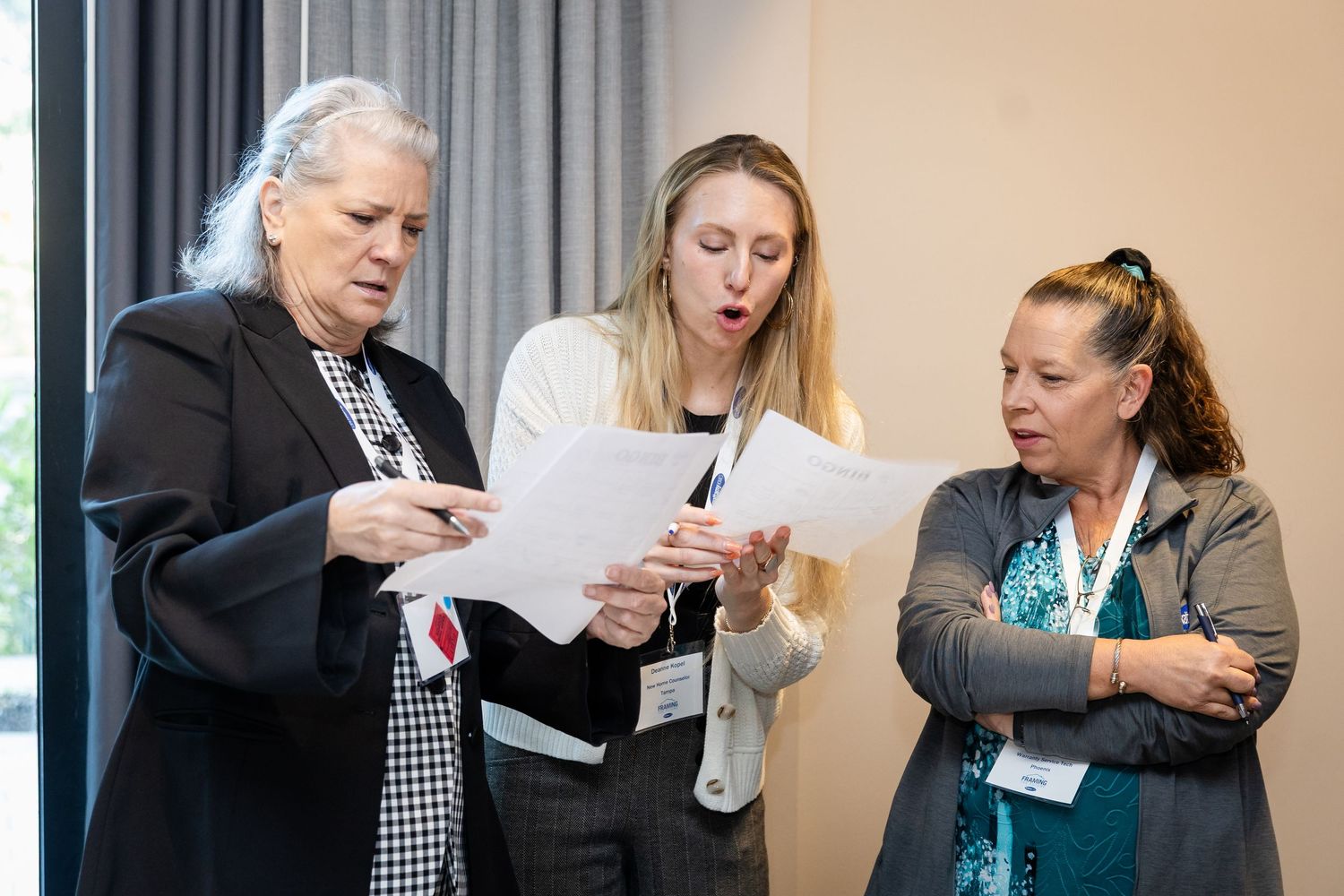 Three professional women reviewing documents together at a business conference or meeting event.