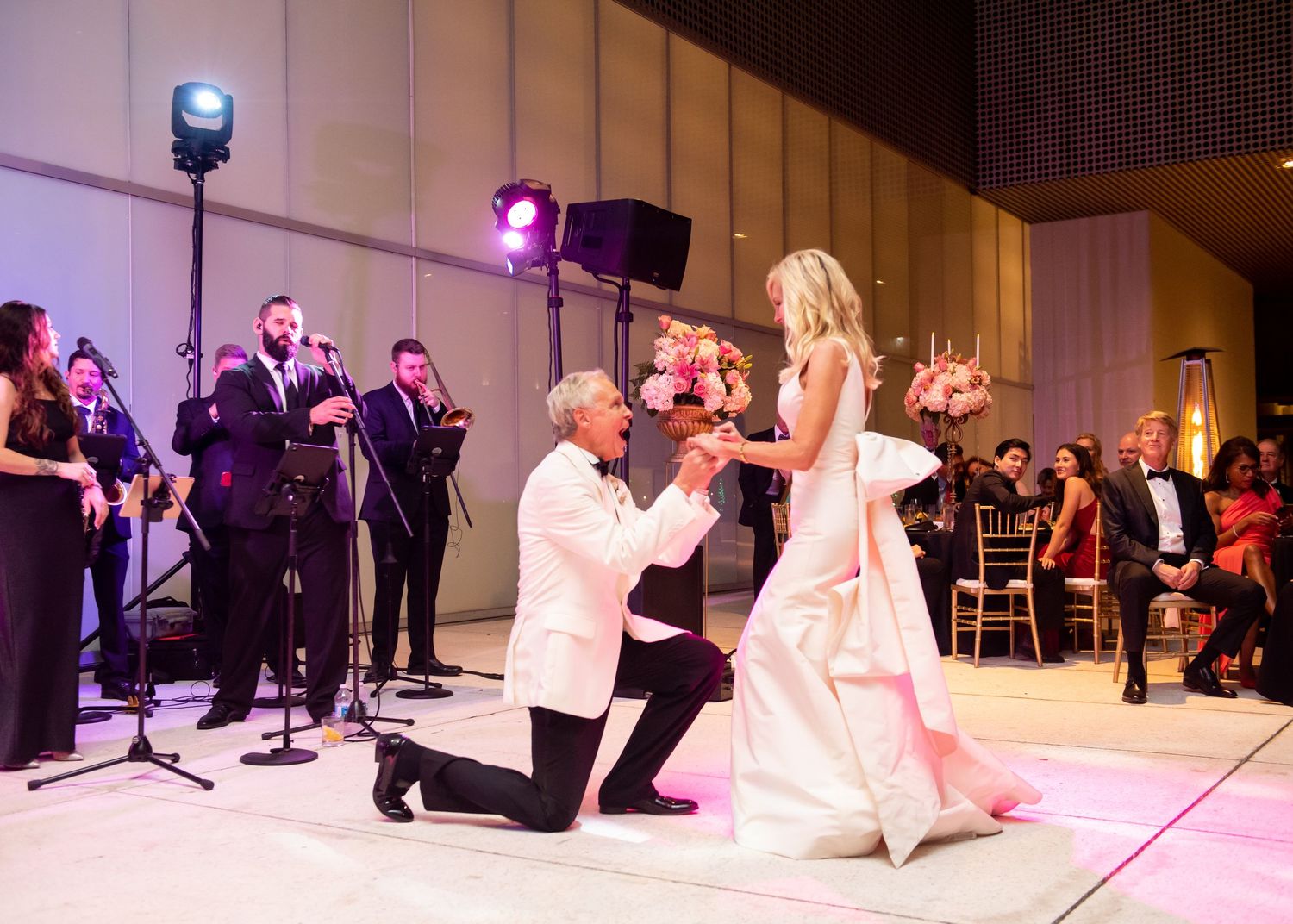 Groom kneels before bride during romantic first dance at elegant wedding reception.