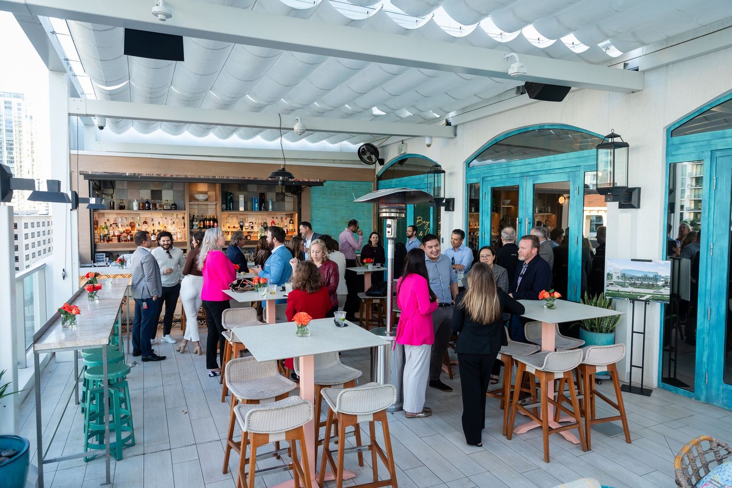 Guests mingle on a bright outdoor patio with teal accents at a social gathering or networking event.