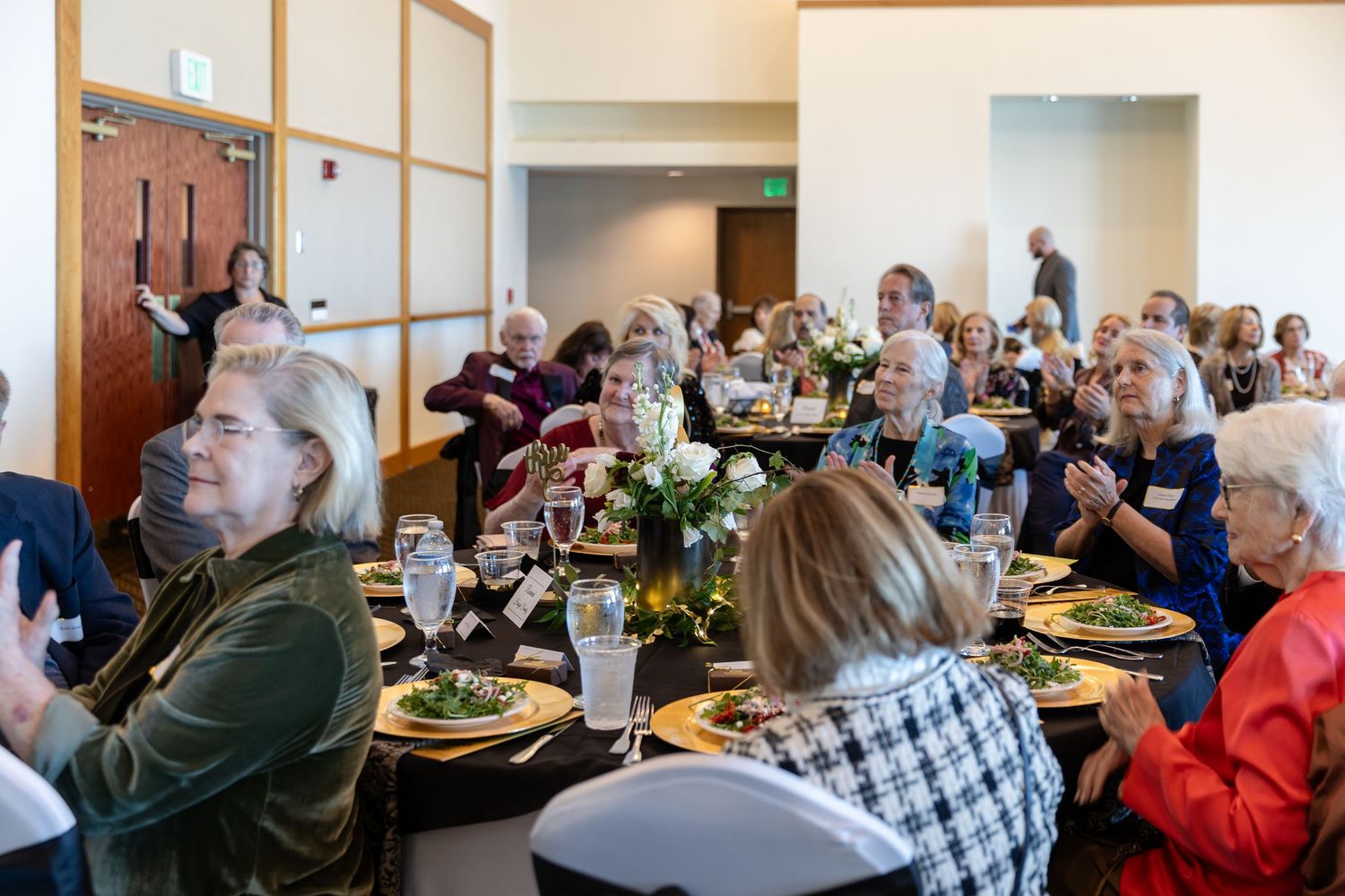 Women gathered around decorated tables enjoying a catered luncheon event in a bright banquet hall.