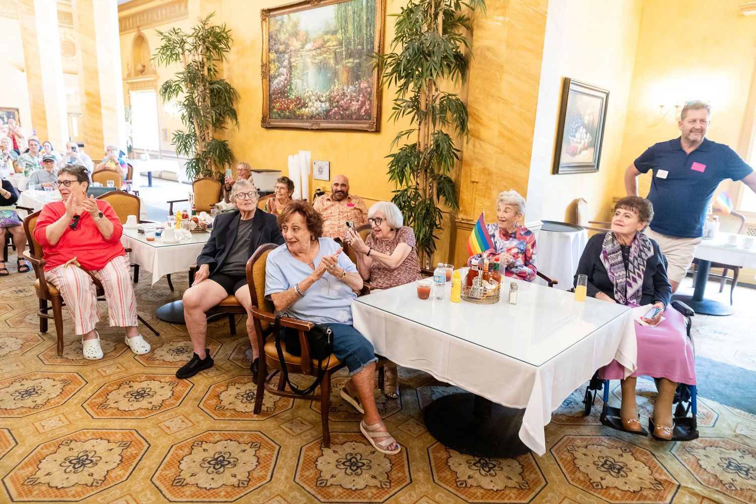 Elderly residents clapping and smiling at a senior living community event in an elegant dining room.