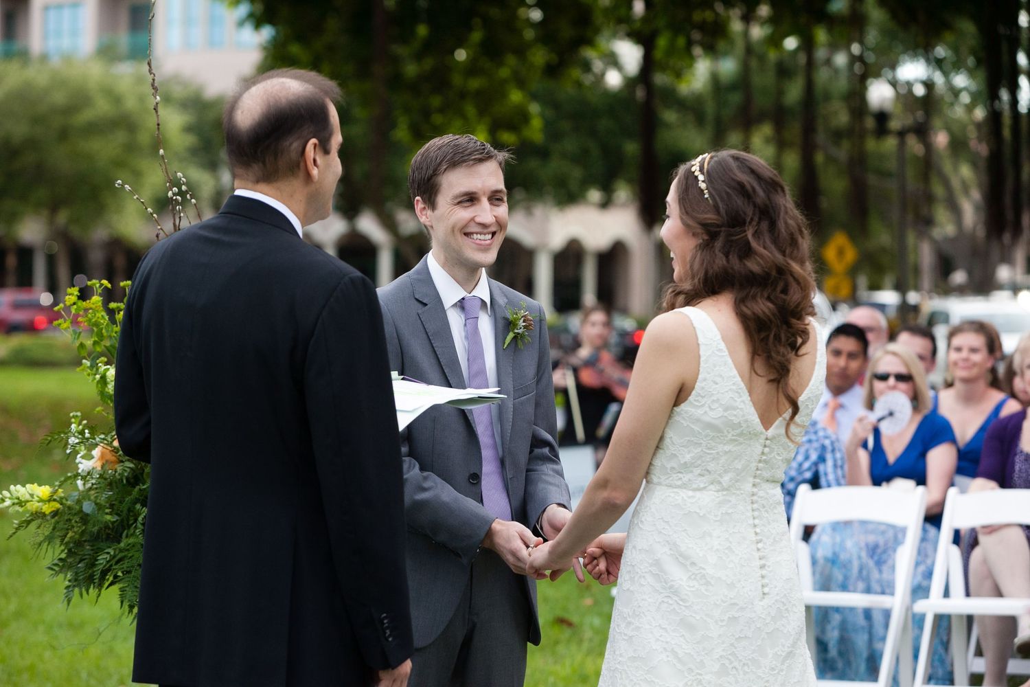 Groom smiles holding bride's hands at outdoor wedding ceremony while officiant reads from paper Museum of Fine Arts, St. Petersburg.