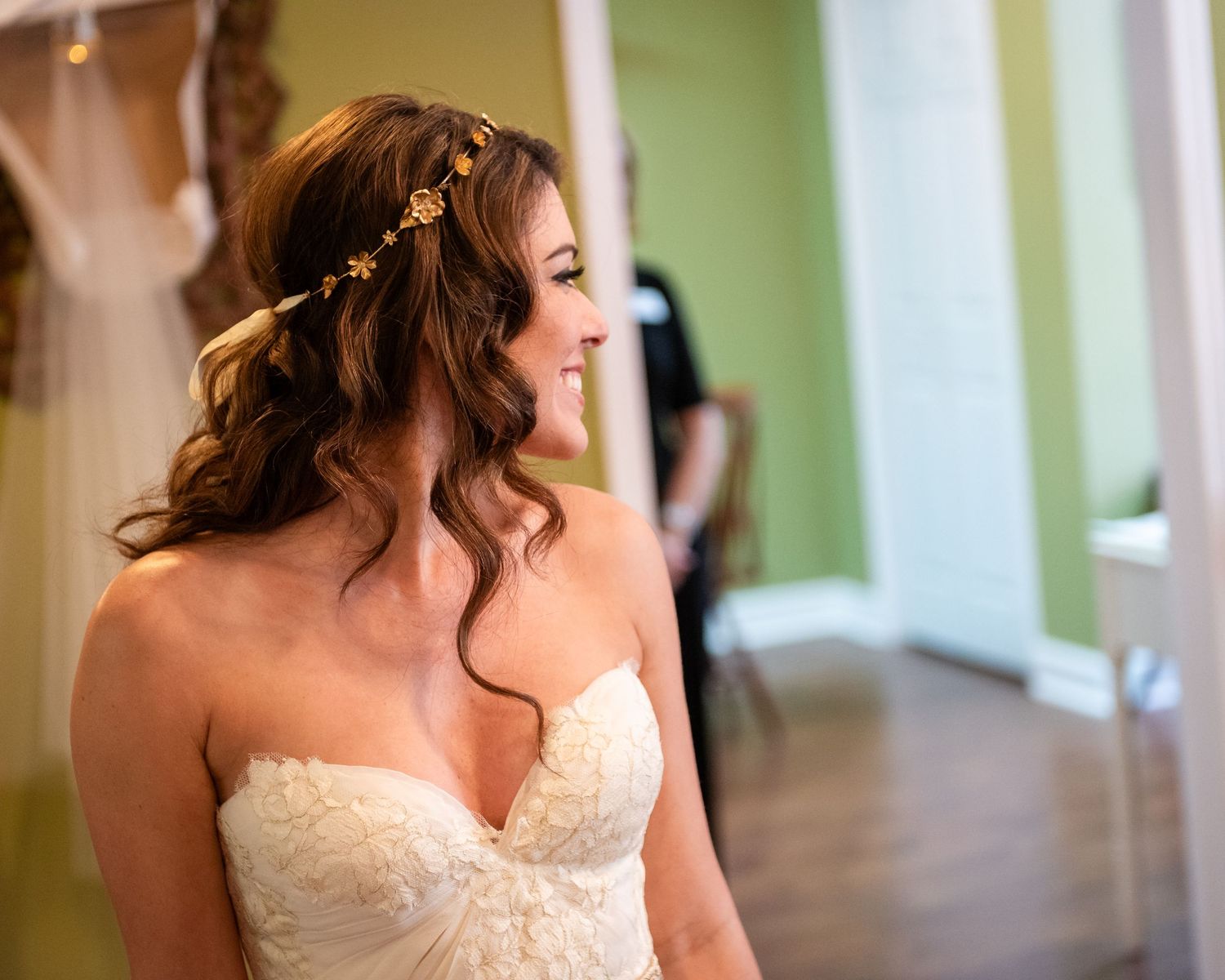 Smiling bride in strapless lace wedding gown wearing gold floral hair crown with elegant half-up hairstyle.