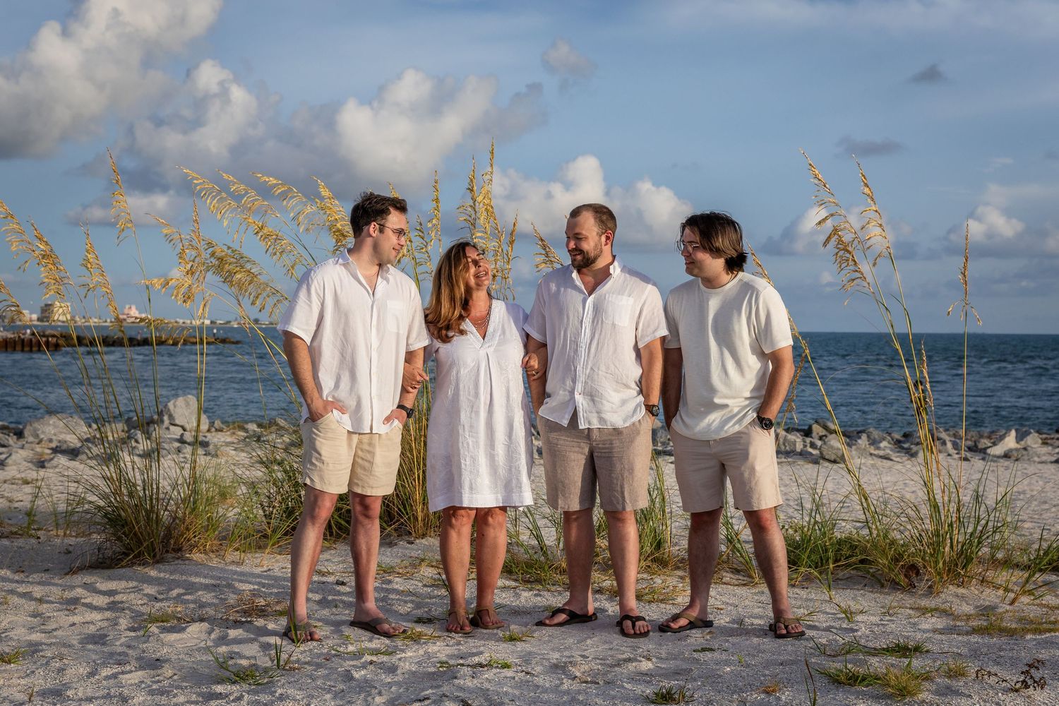 Family of four posing on a sandy beach with sea oats and ocean views on a sunny day.