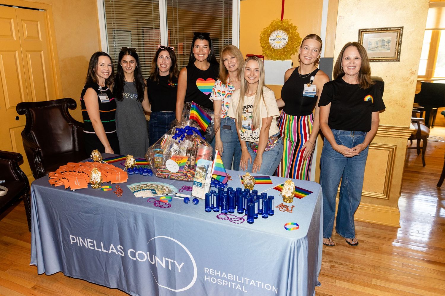 Group of women posing at a Pinellas County Rehabilitation Hospital event table with colorful decorations and blue bottles.