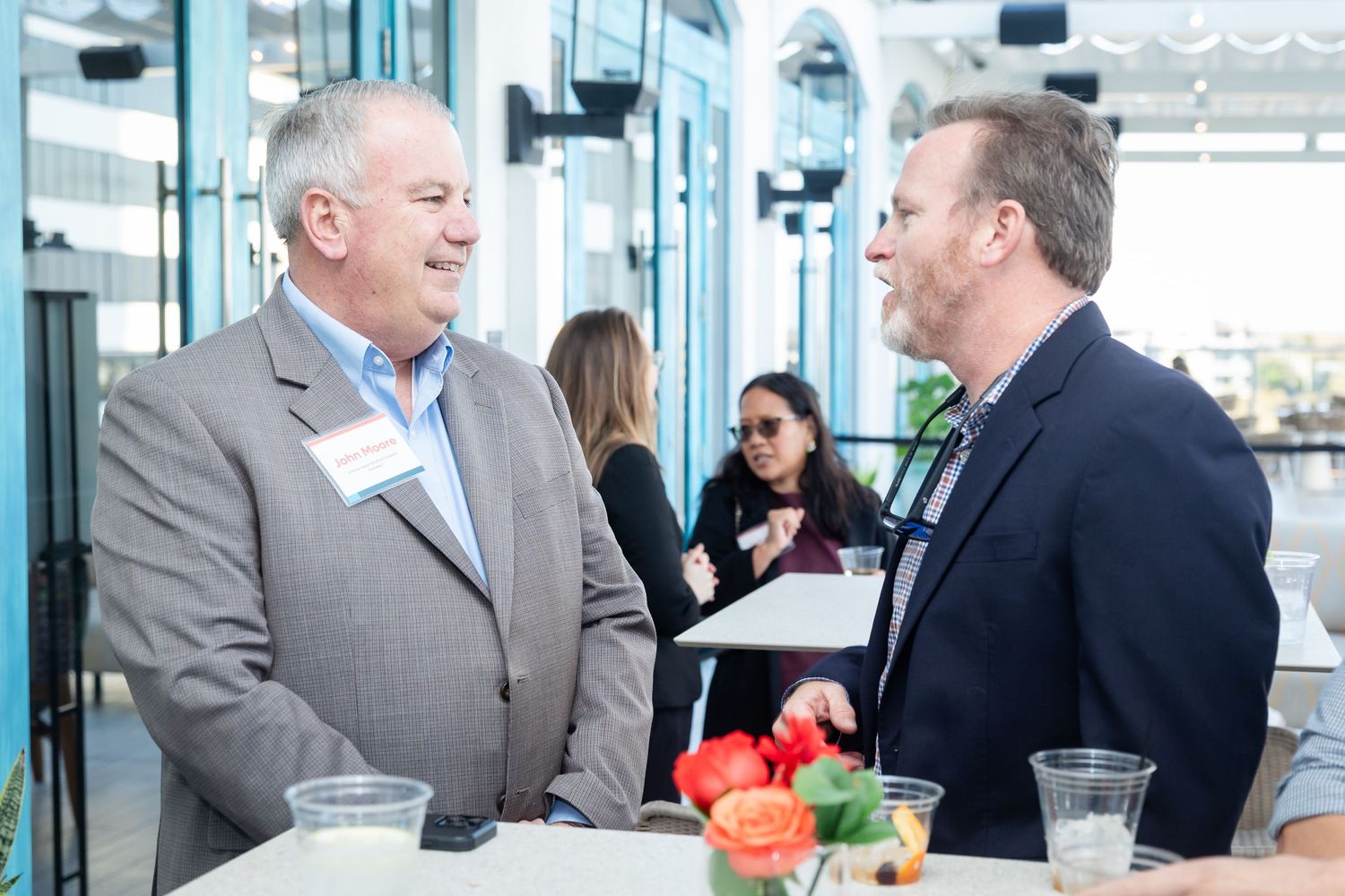 Two men in business attire networking and conversing at a standing table during a corporate event.