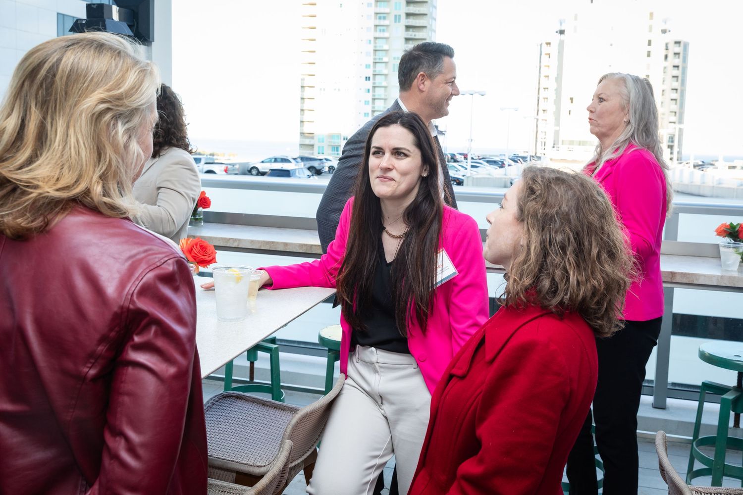 A group of women in colorful attire socialize at a rooftop networking event with city views.