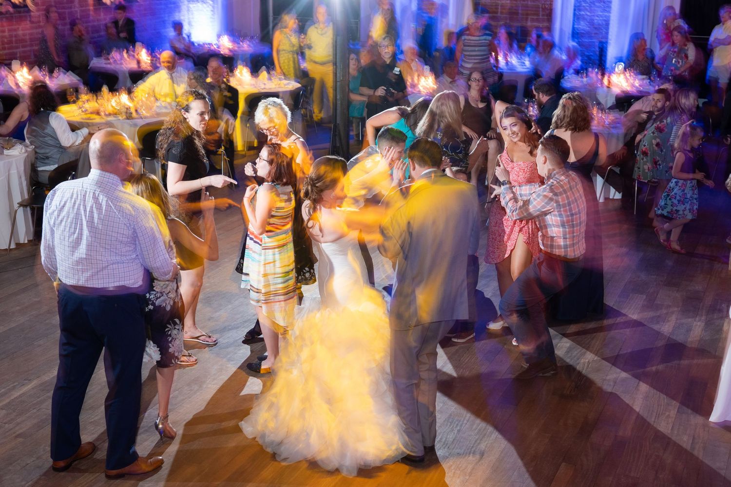 Bride and groom share first dance surrounded by celebrating guests at vibrant wedding reception.