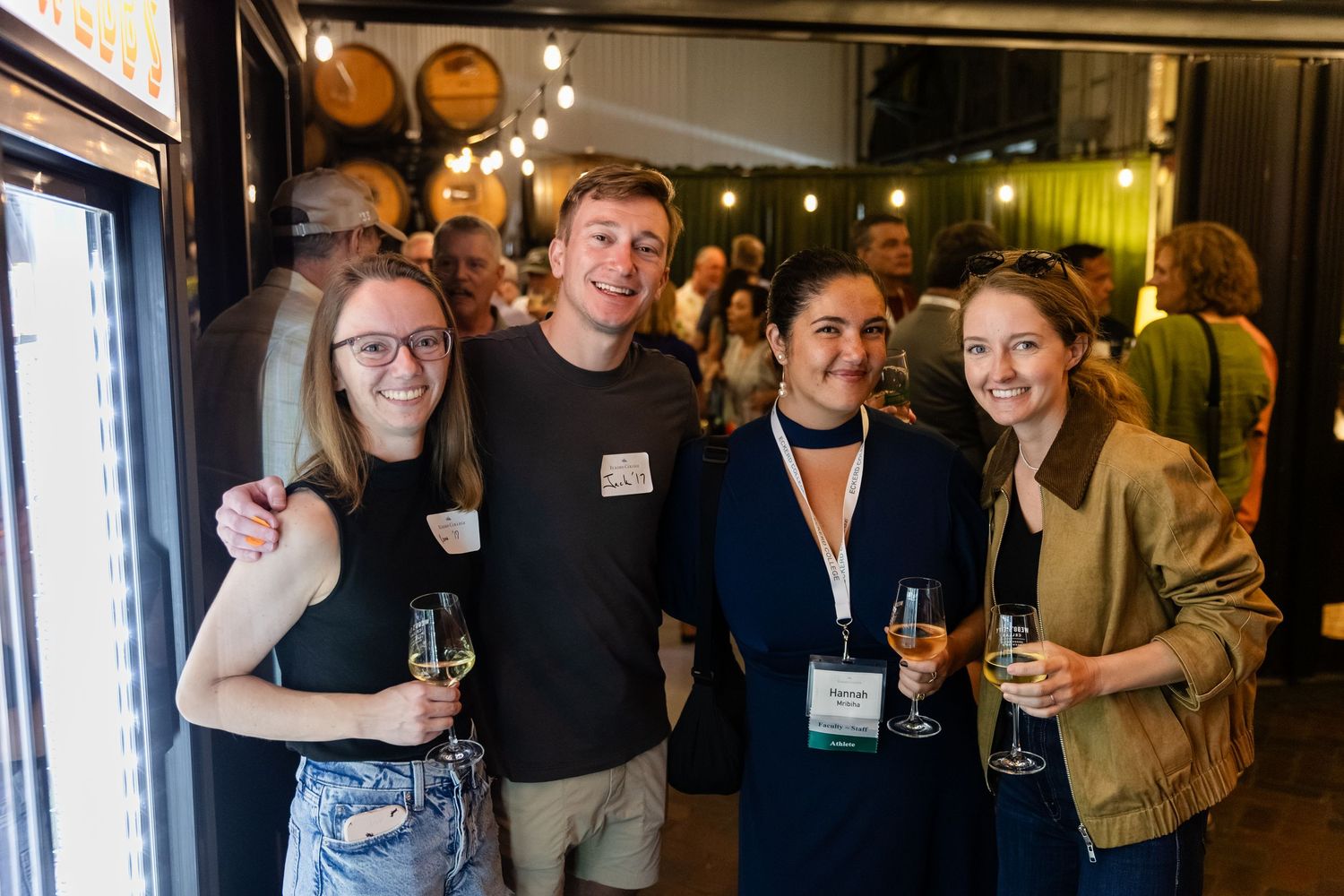 Four young adults smile holding wine glasses at a brewery networking event.