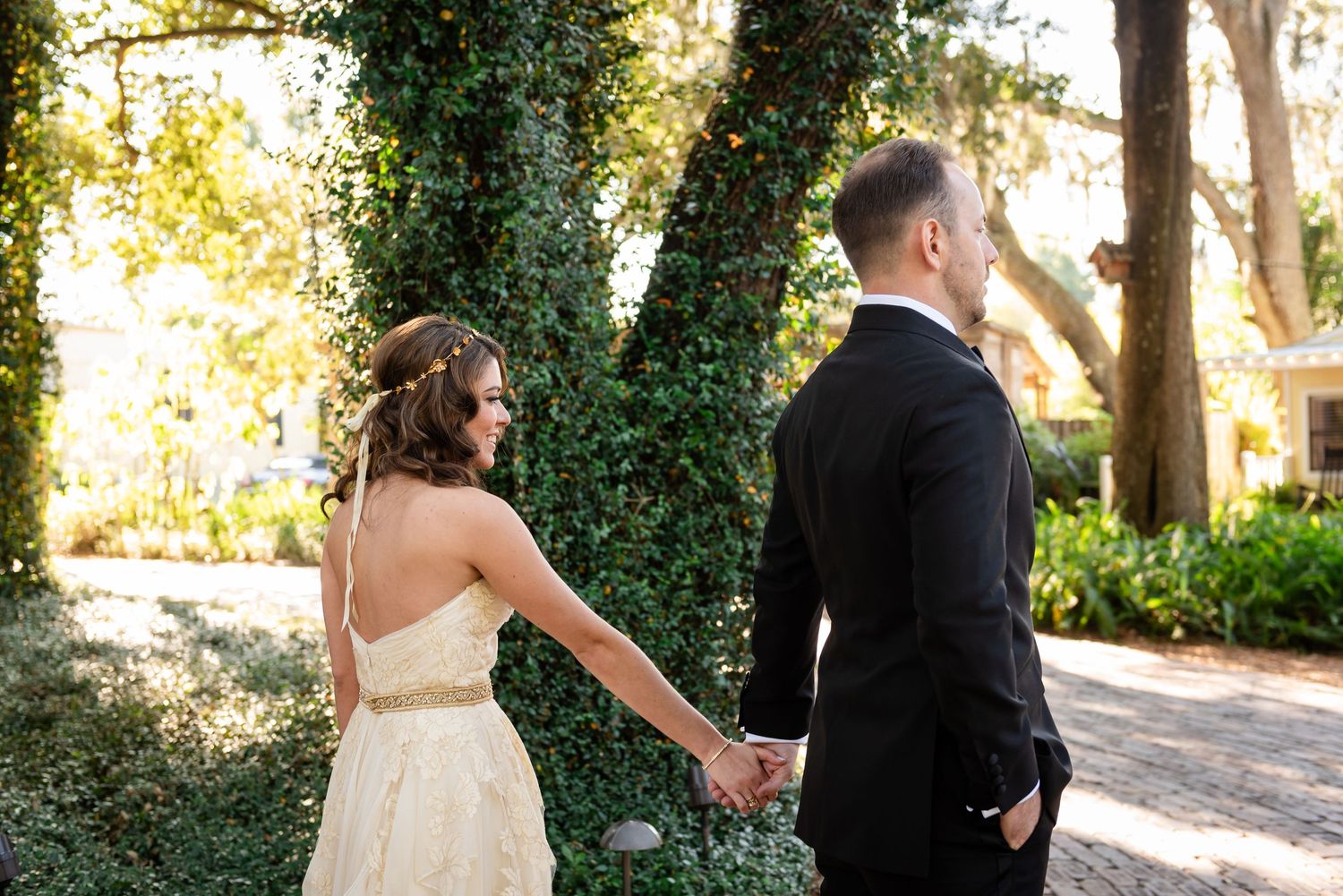 Bride and groom holding hands outdoors near ivy-covered wall before wedding ceremony.
