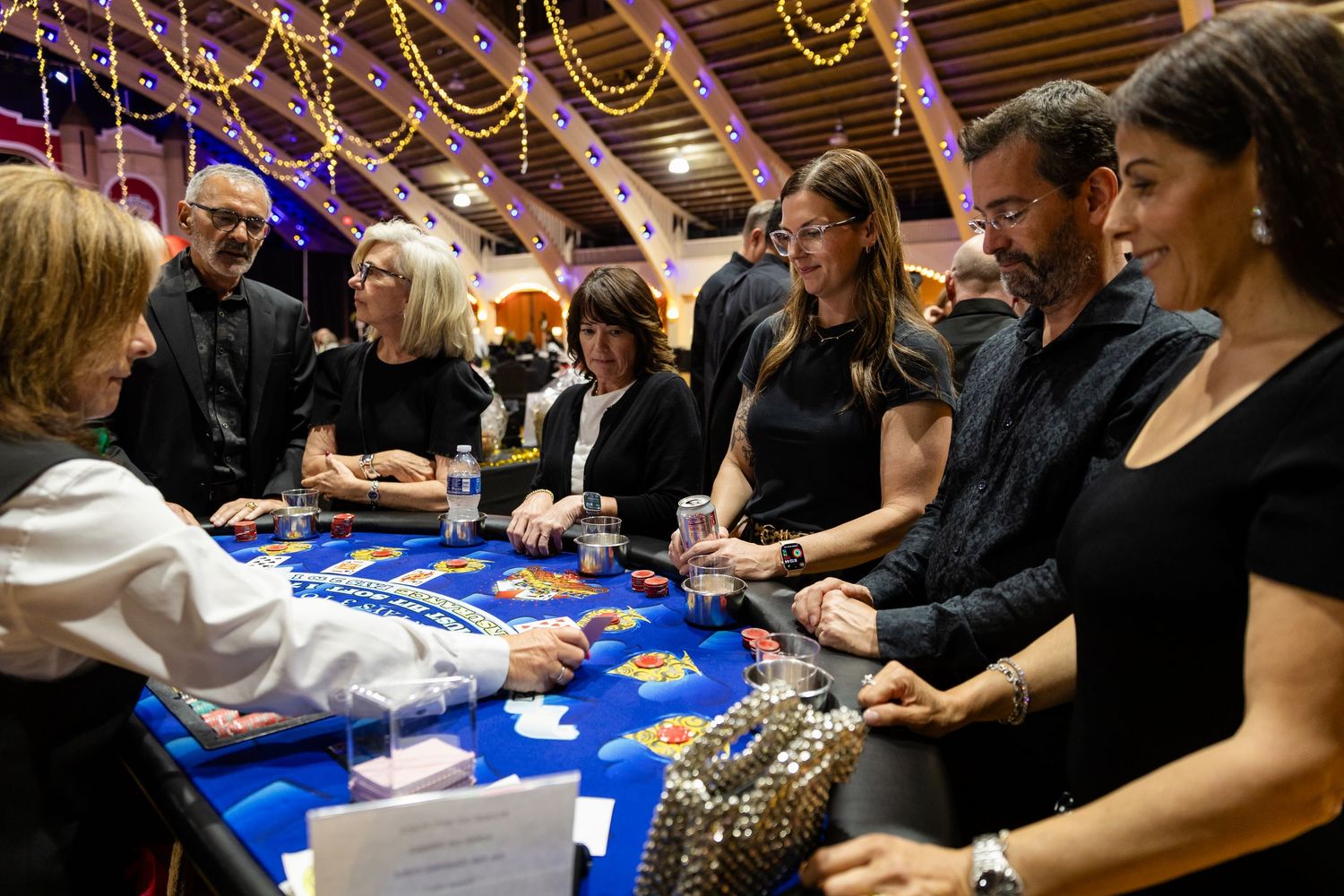 A group of elegantly dressed guests playing blackjack at a festive casino night charity event.