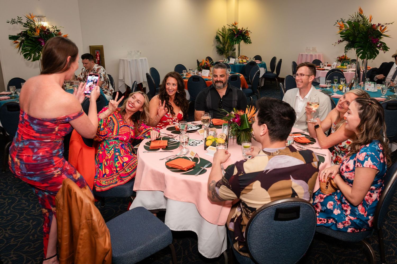 Group of friends posing and taking photos at a festive dinner table during a tropical-themed banquet event.