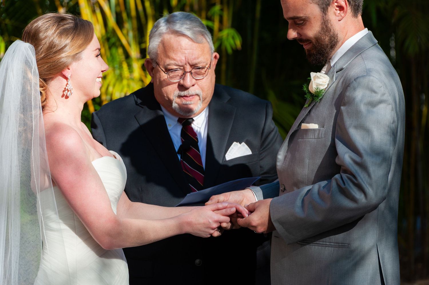 Officiant joins bride and groom hands during outdoor ring exchange.