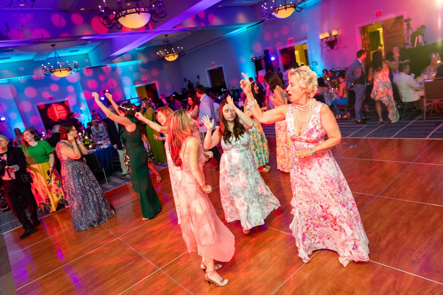 Women in elegant gowns dancing joyfully on a colorful dance floor at a formal event.