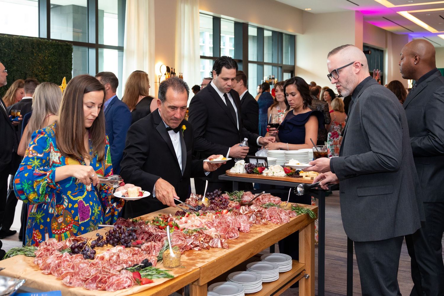 Guests in formal attire serve themselves at an elegant charcuterie buffet during an upscale corporate event reception.