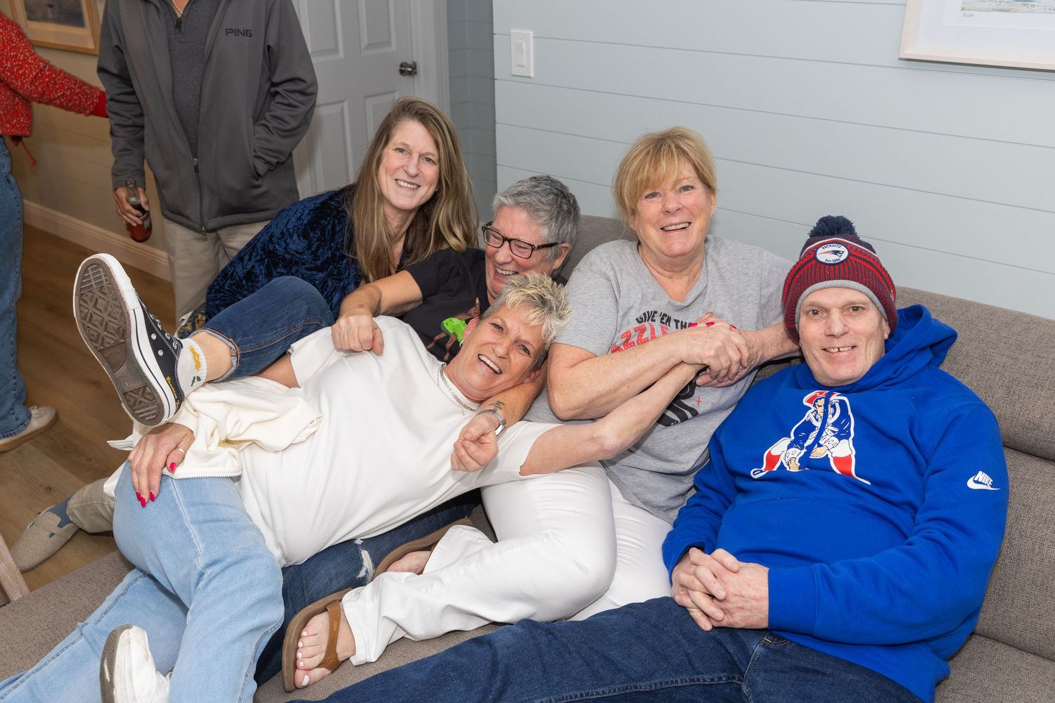 Group of five friends laughing and posing together on a cozy living room couch.