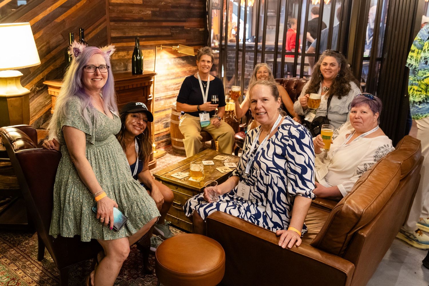 Group of women smiling and posing together in a cozy wood-paneled bar lounge, holding drinks at a social gathering.