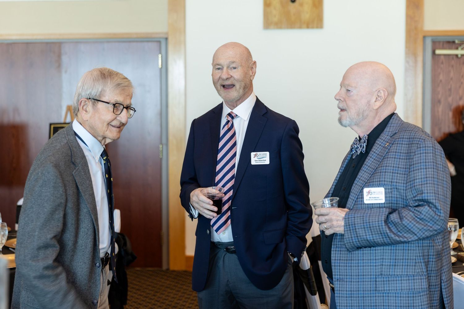 Three professional men in suits conversing at a corporate networking event or business reception.