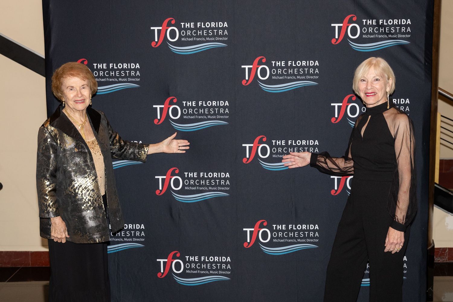 Two women pose in front of The Florida Orchestra branded step-and-repeat banner at formal gala event.
