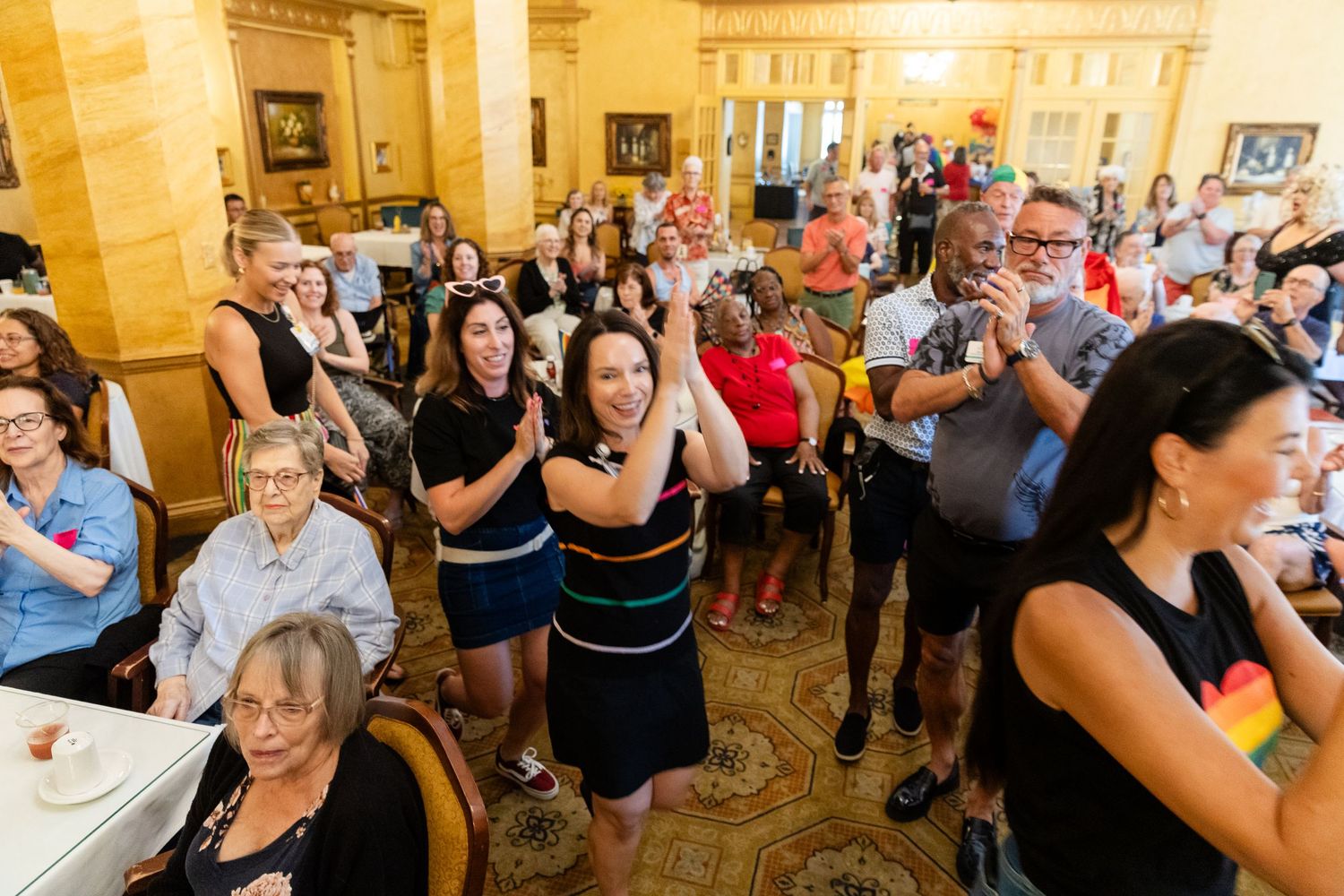 Diverse crowd of people clapping and celebrating enthusiastically at a lively indoor community event.