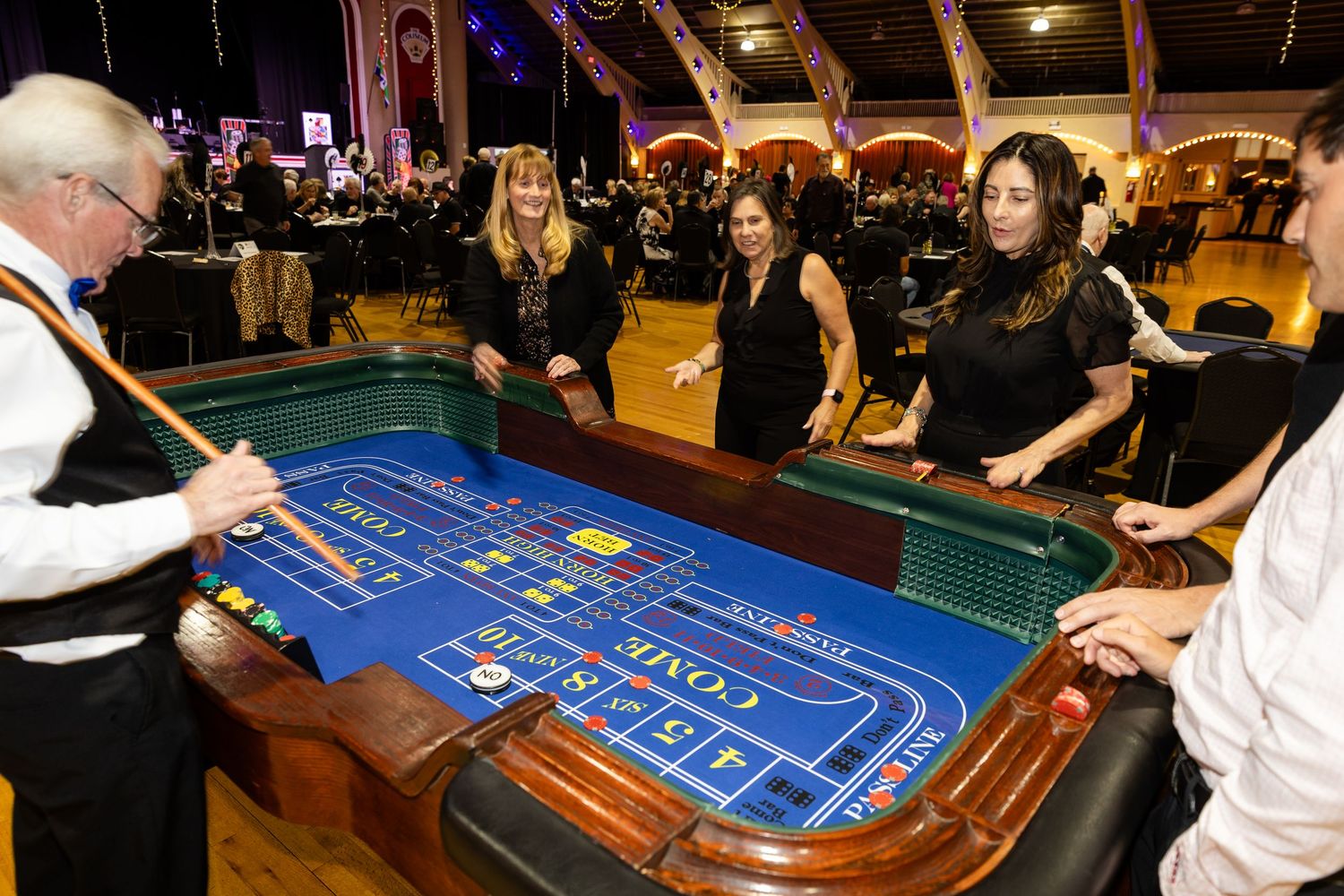Women in black dresses playing craps at a casino table during a formal event.