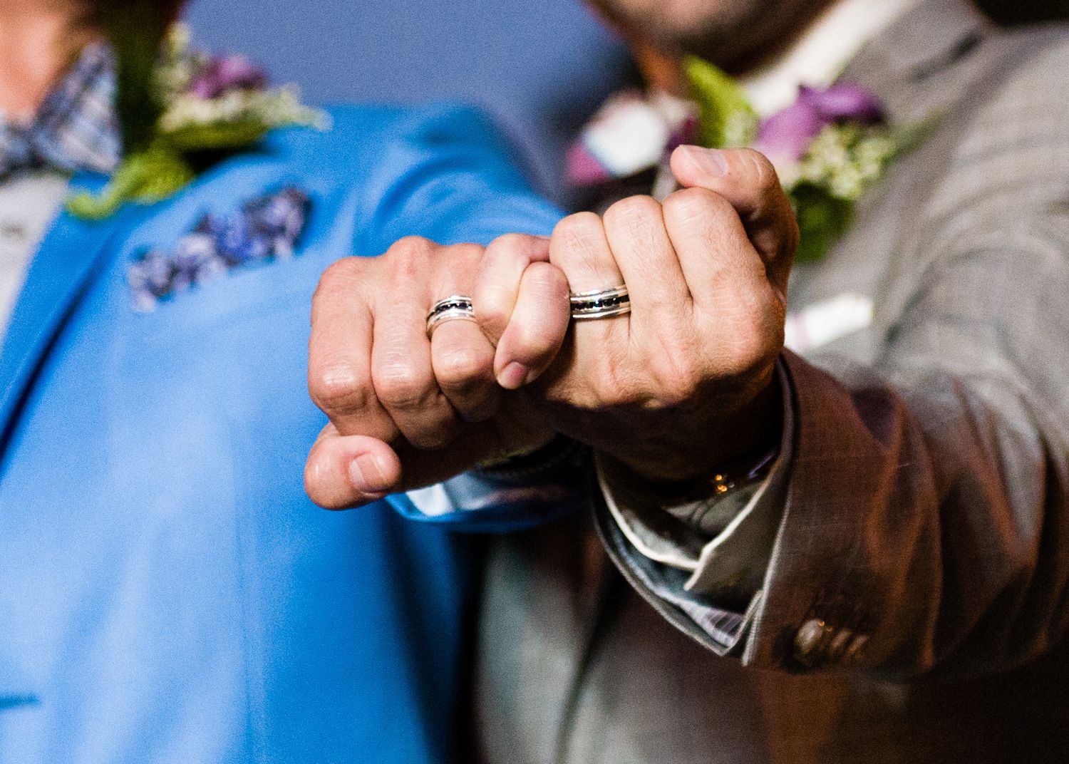Close-up of two grooms showing off wedding rings with fist bump pose at wedding ceremony.